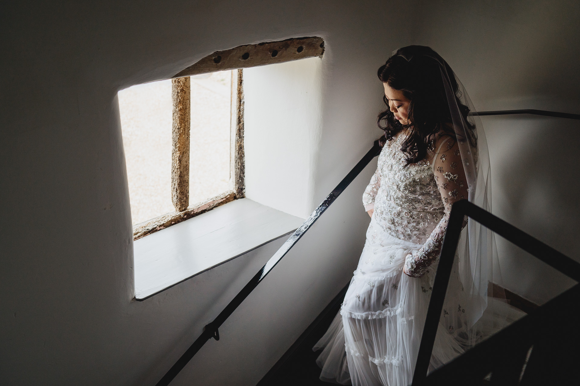 a bride walking down a staircase with window light
