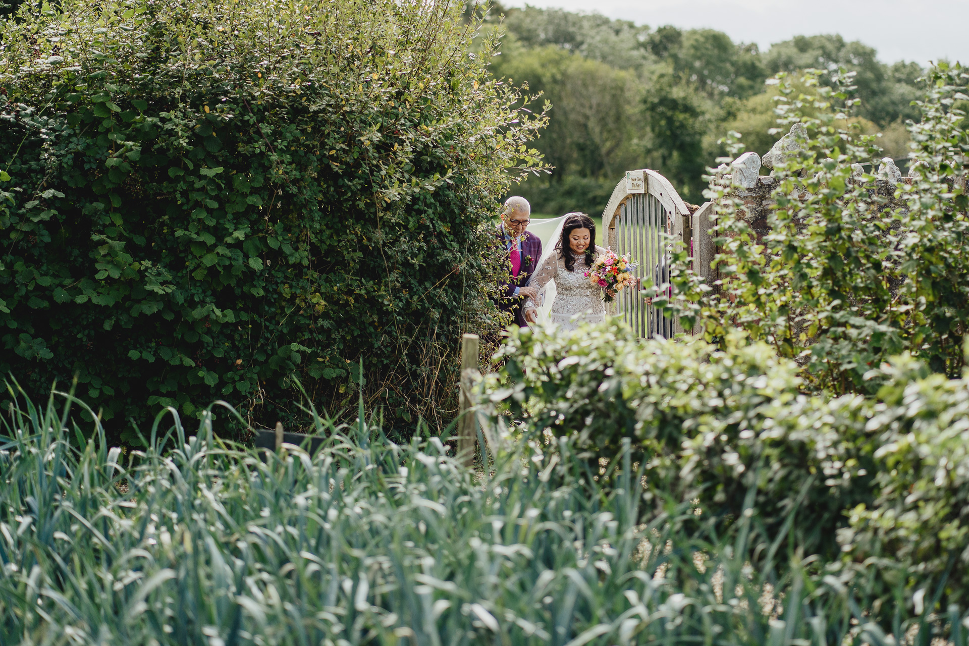 a bride and her father arriving for a wedding ceremony, walking through a kitchen garden