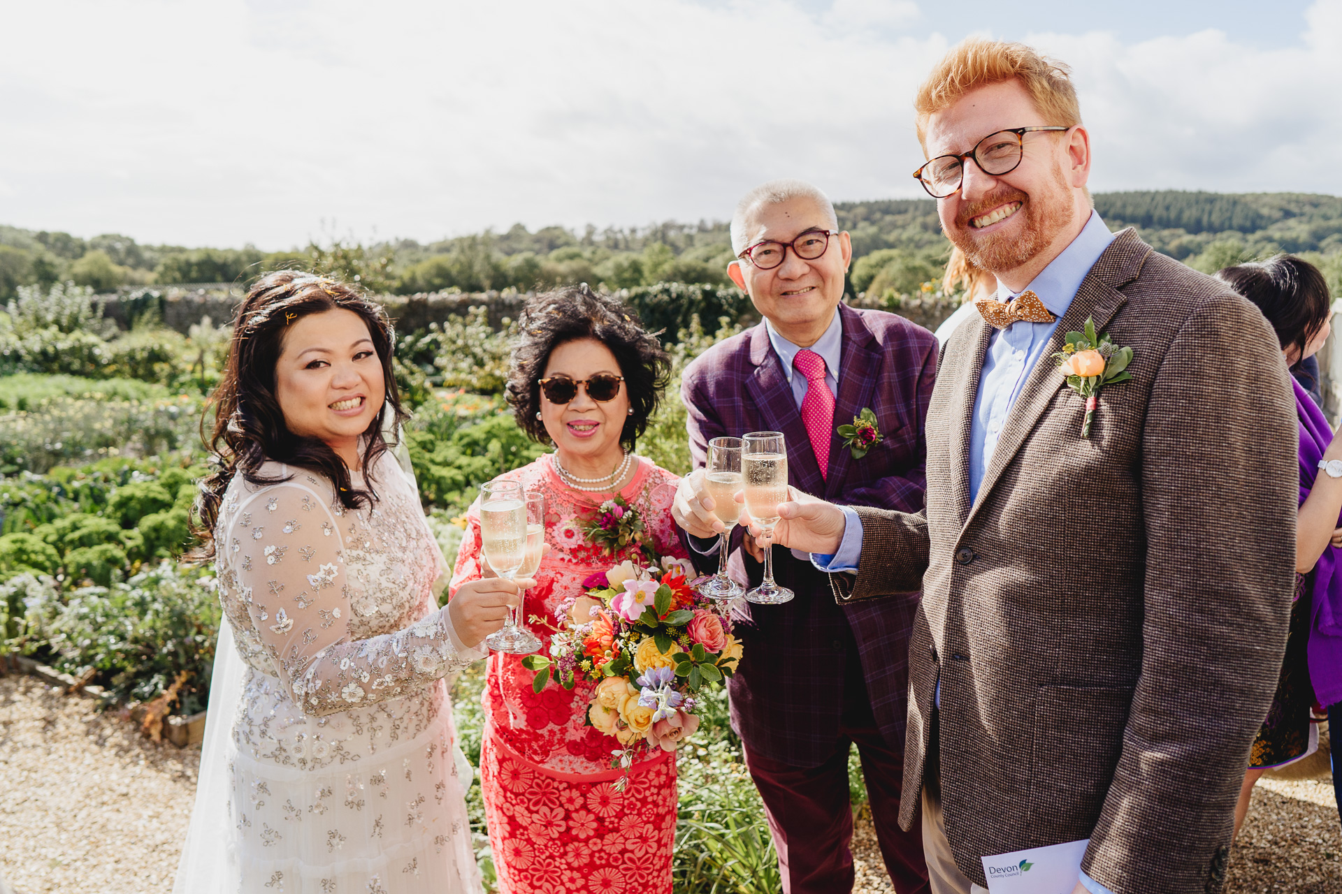 bride and groom clinking glasses with parents outdoors in a kitchen garden