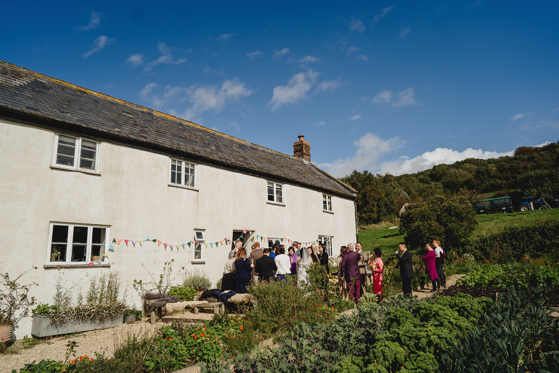 wedding guests outside river cottage farmhouse with blue skies above