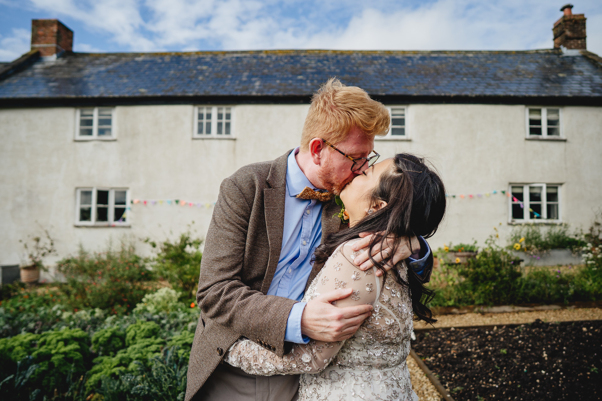 bride and groom kissing with farmhouse behind them