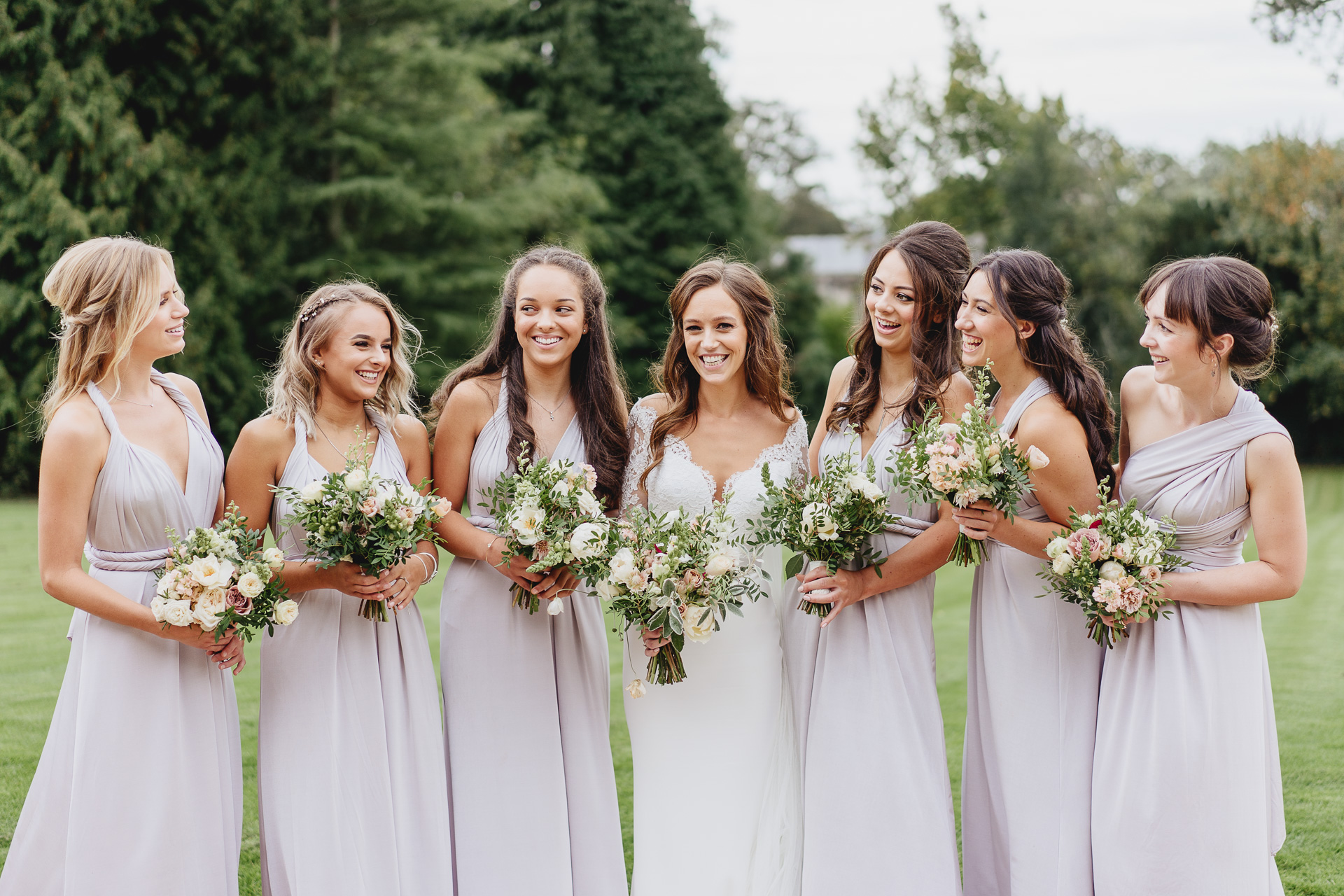 Bride and bridesmaids group shot on the grass with trees behind