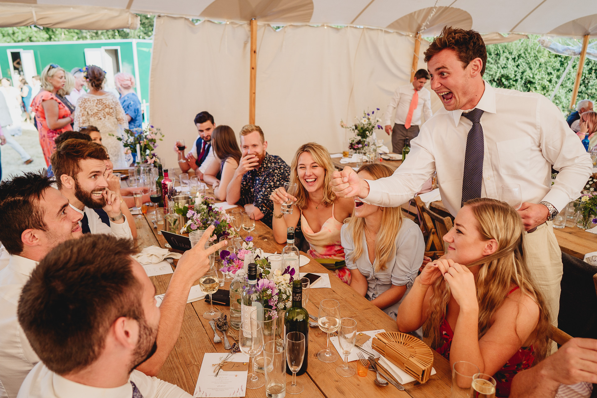 Wedding guests laughing together around a table in a marquee
