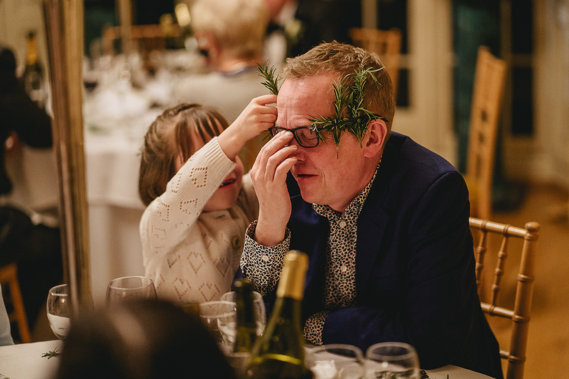 Child placing pieces of rosemary behind a man's glasses