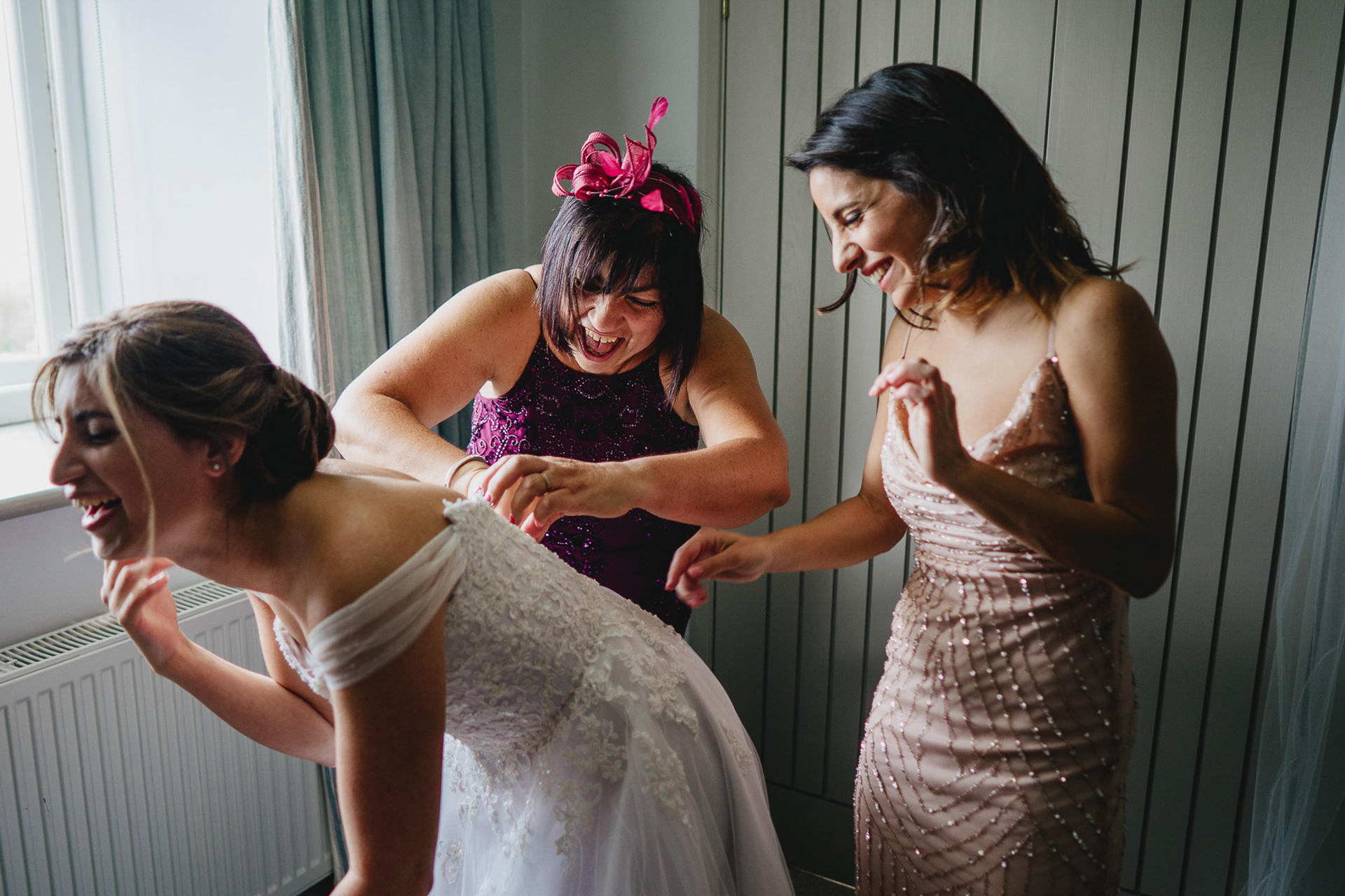 Three women laughing together putting on a wedding dress