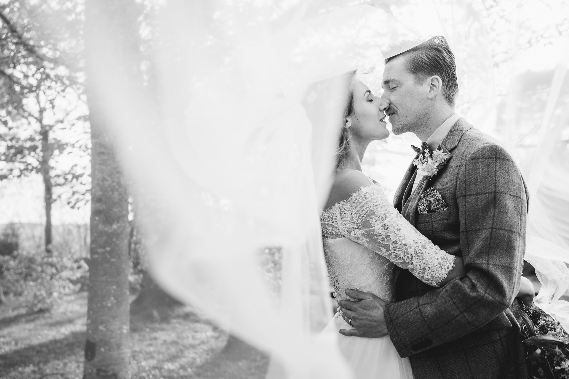 Man and woman kissing underneath a bridal veil