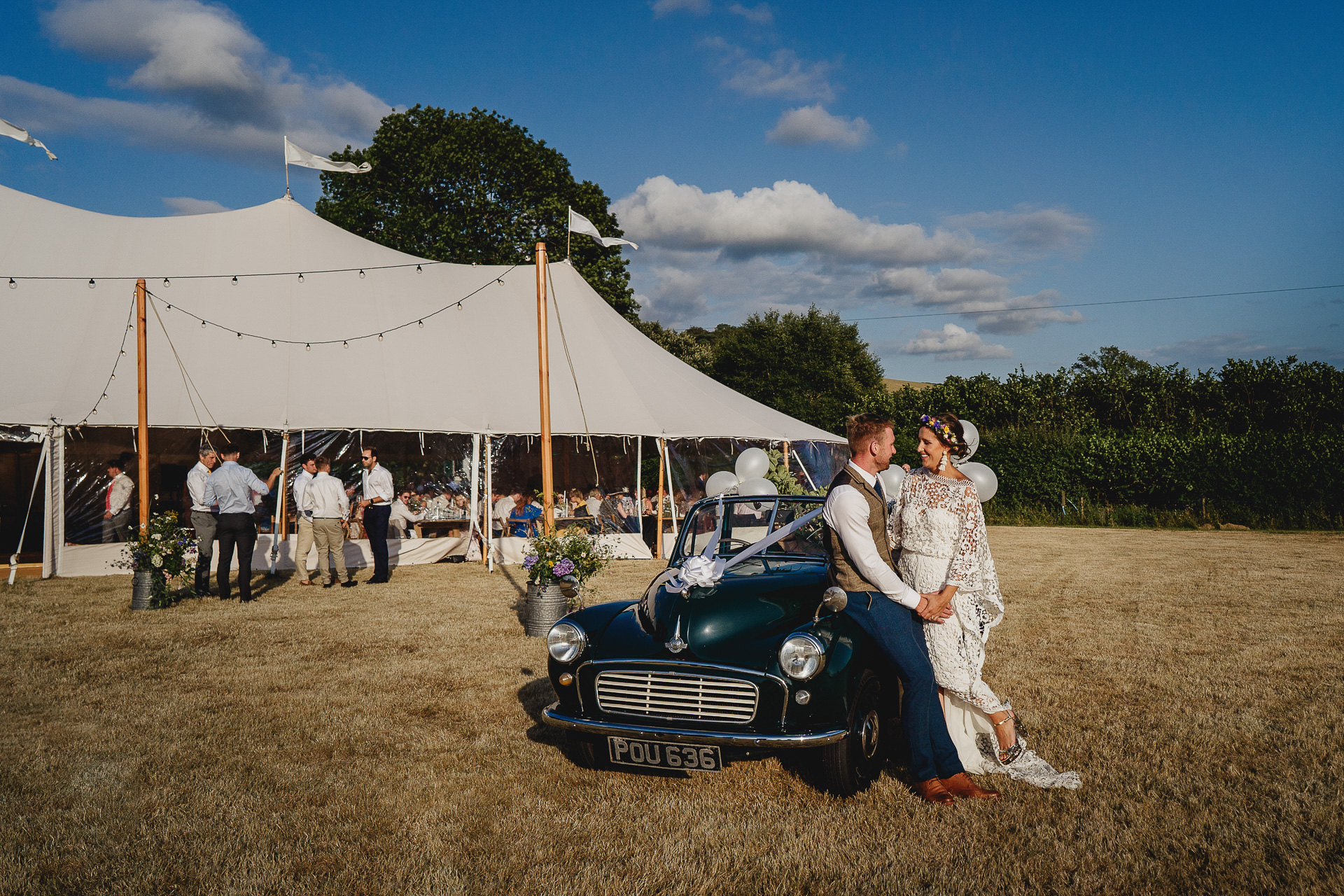 Bride and groom sitting on Morris Minor outside a marquee