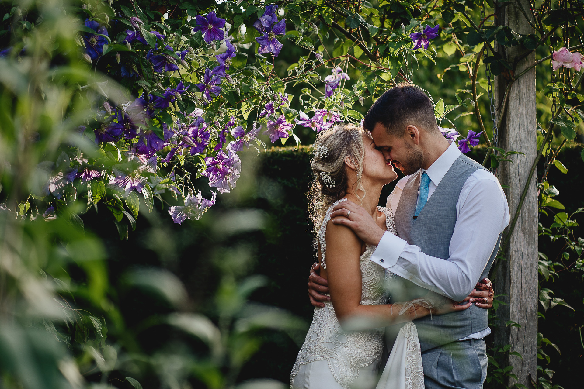 Bride and groom kissing under purple clematis