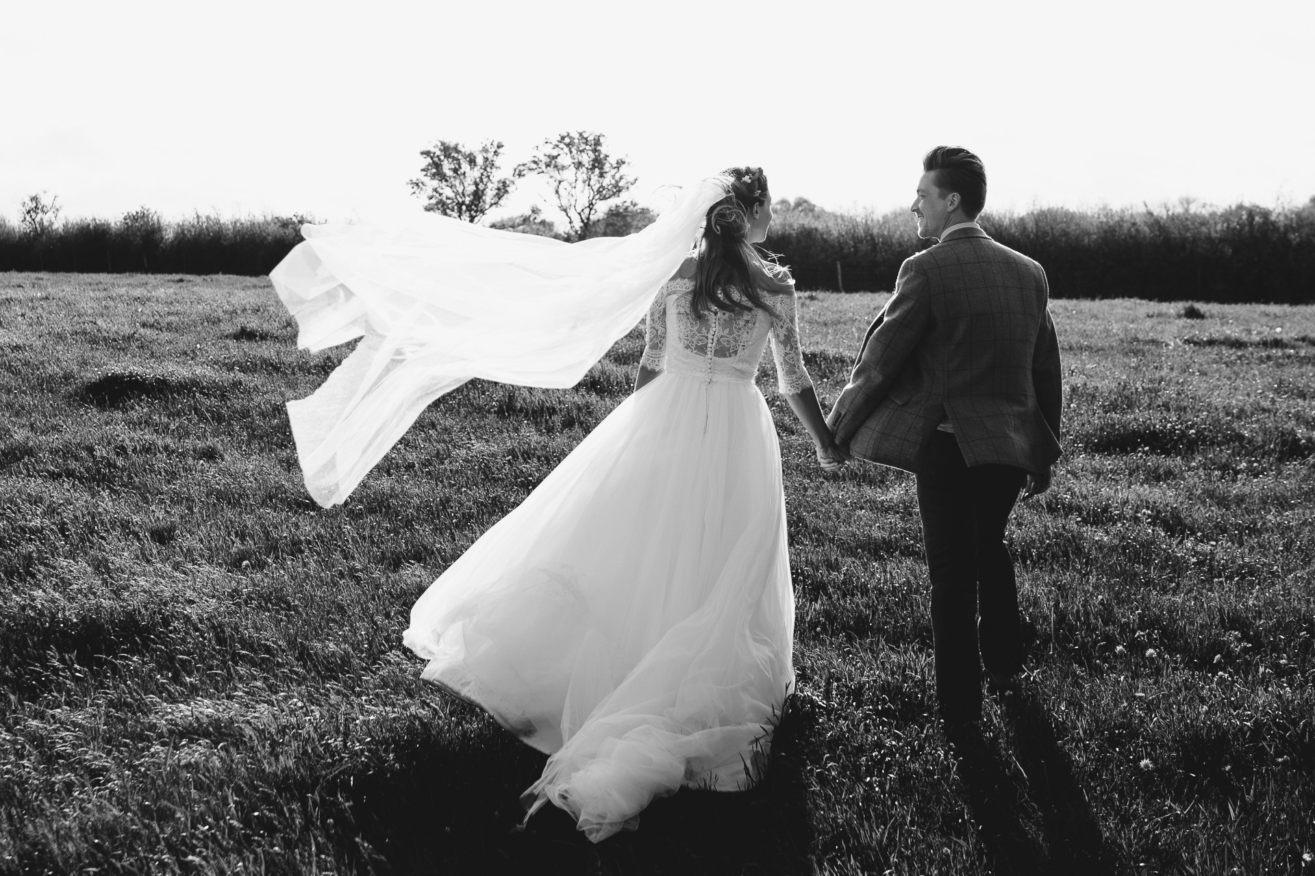 Bride and groom walking through a field and smiling at each other