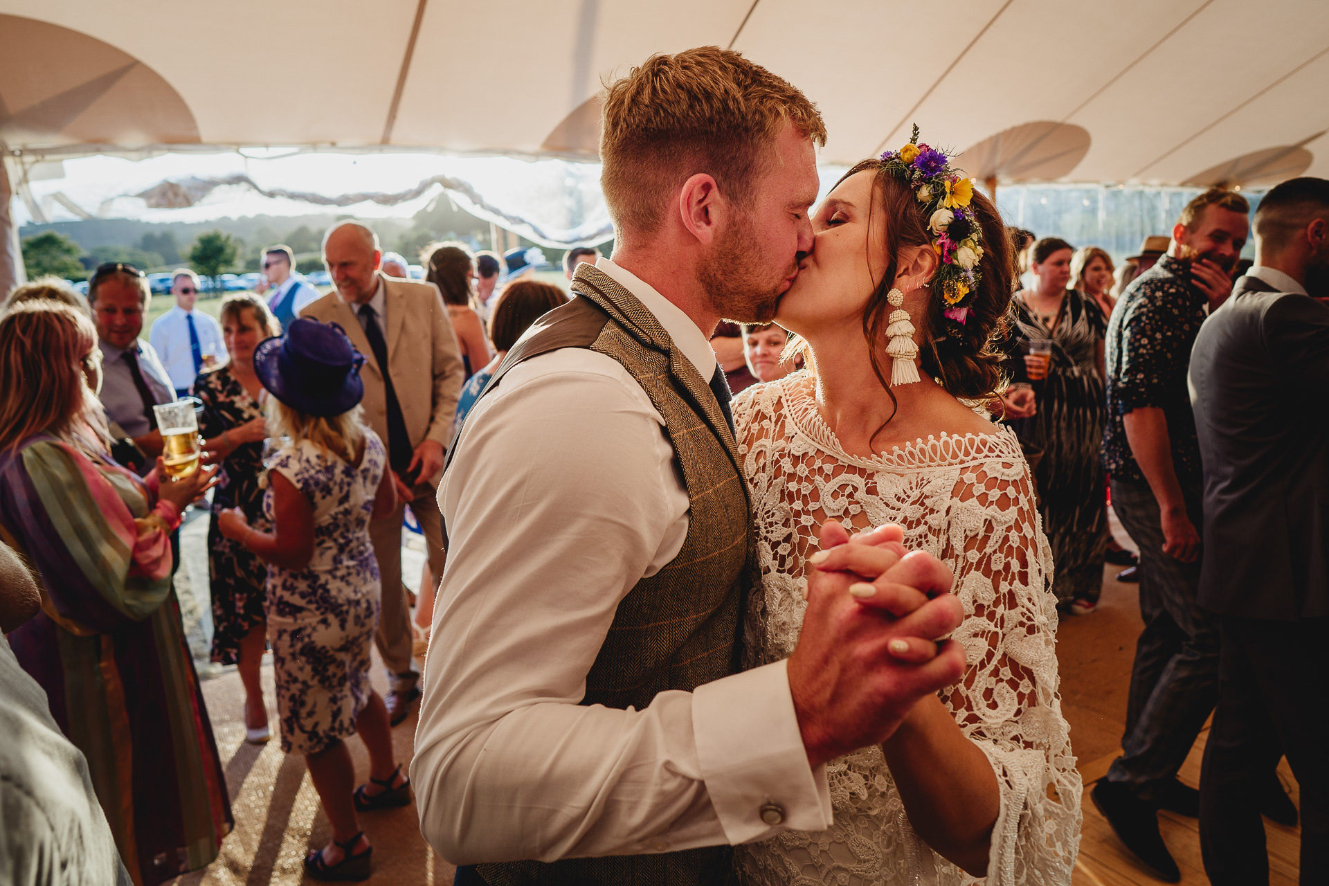 Bride and groom kissing amongst wedding guests in a marquee