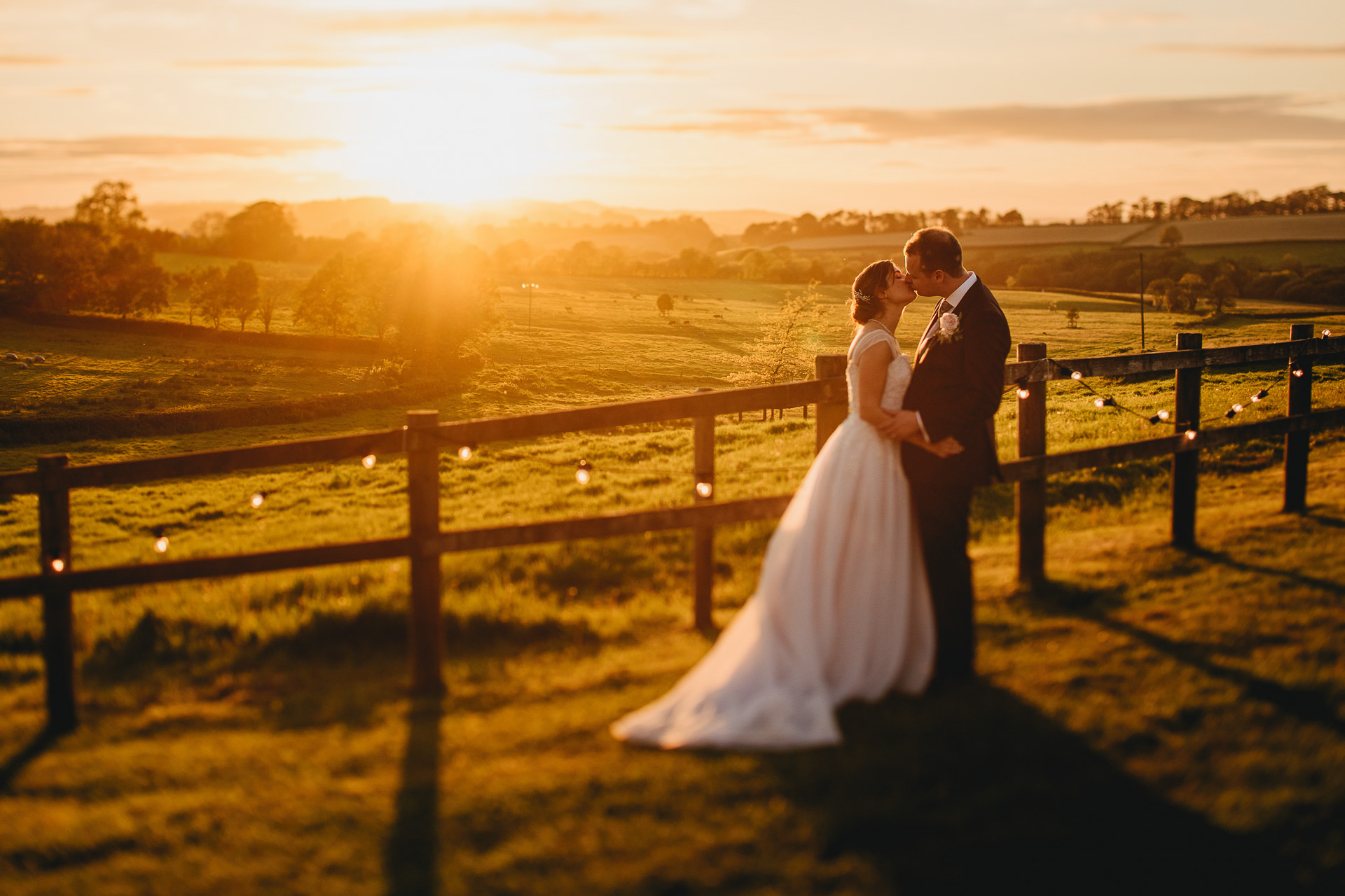 Bride and groom kissing with a sunset and countryside hills behind