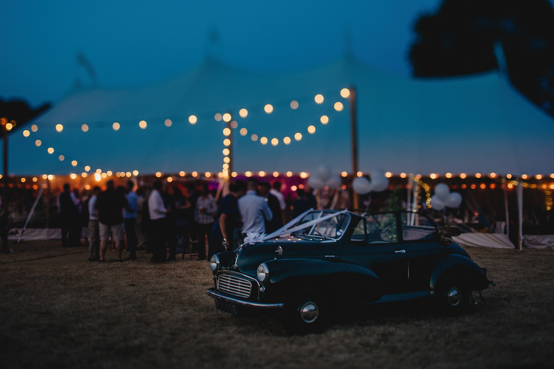 Morris Minor wedding car parked outside a marquee with festoon lighting