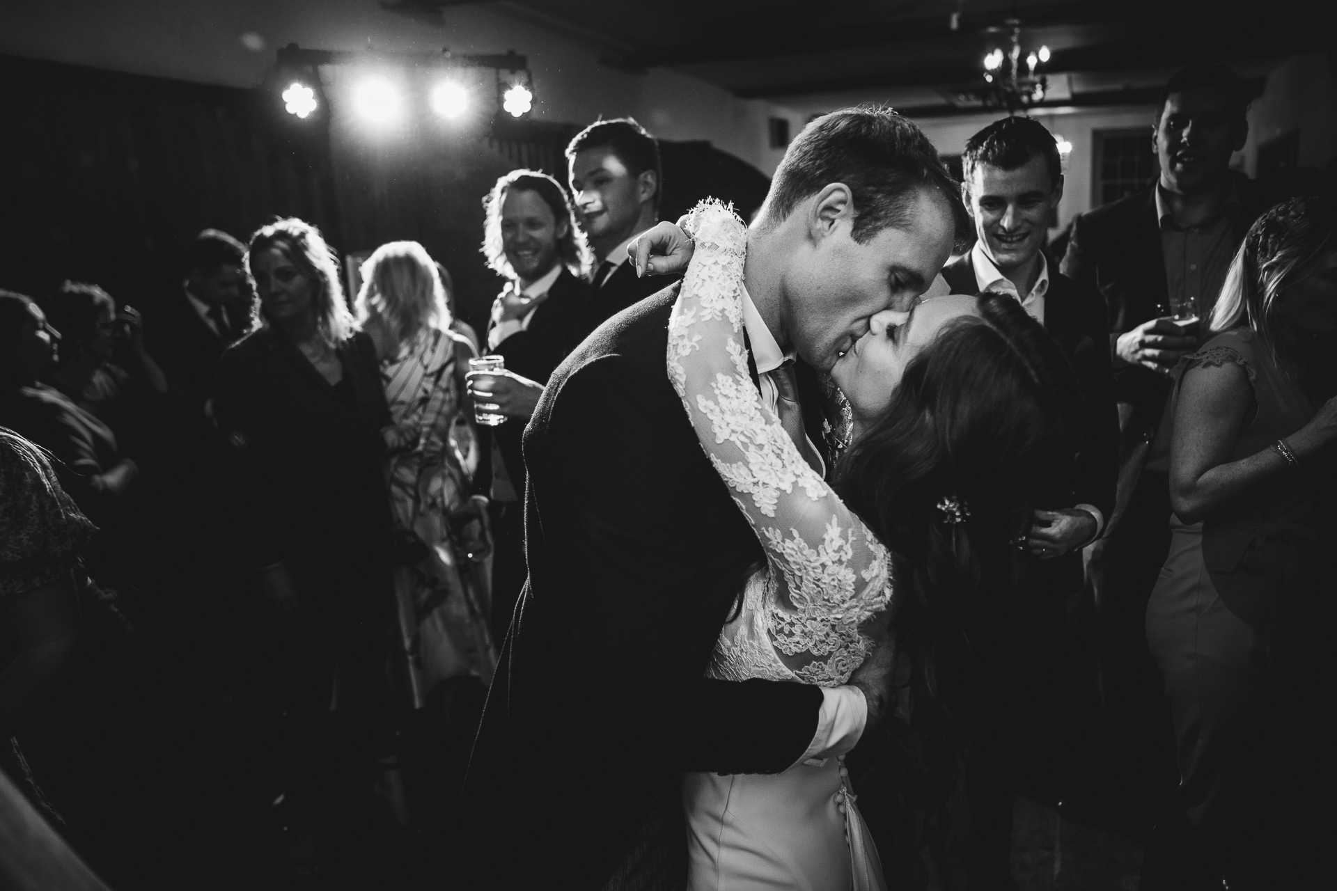 A bride and groom kissing on a dance floor surrounded by other people