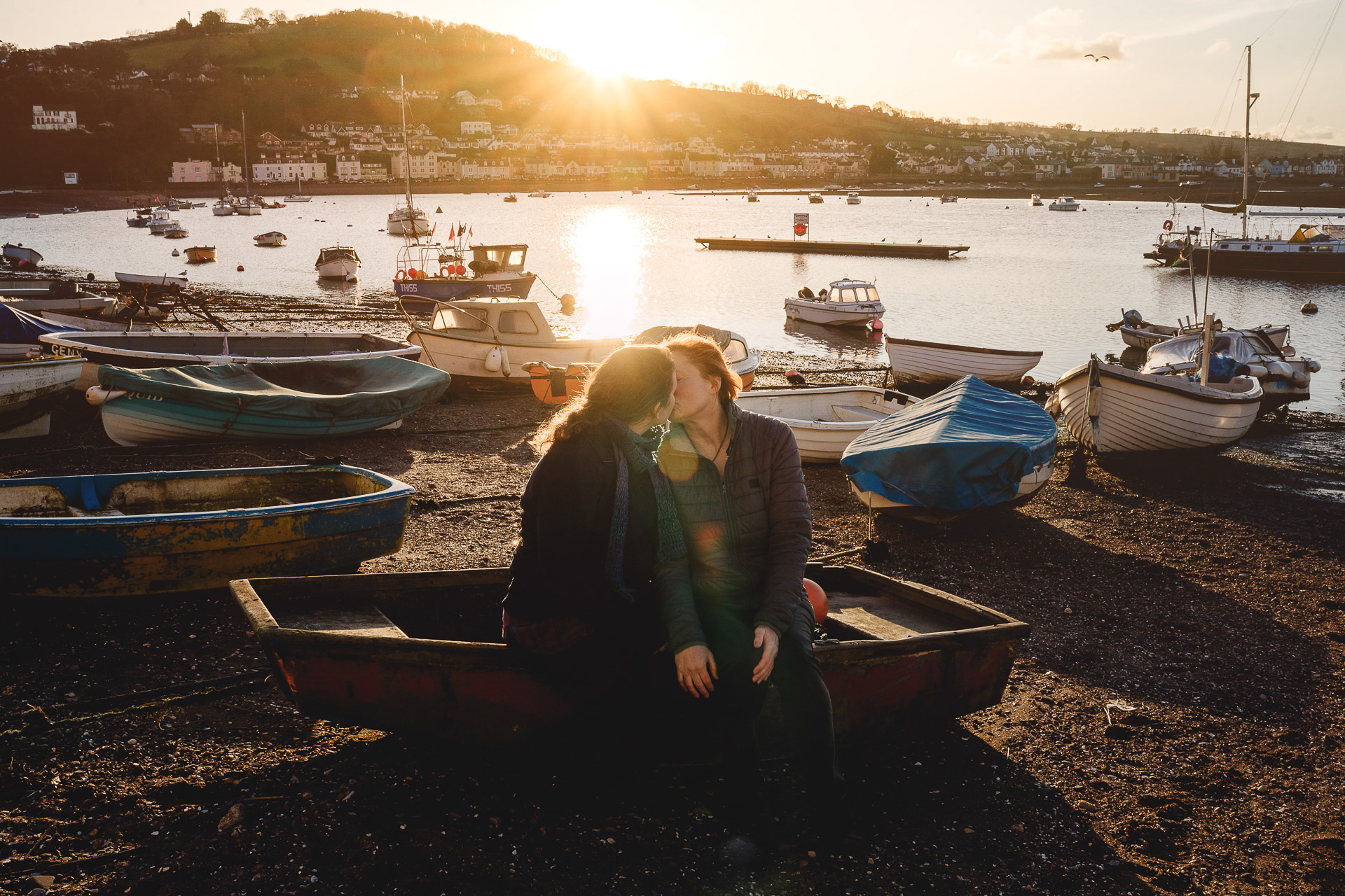 Two women sitting on a boat together kissing in a sunset