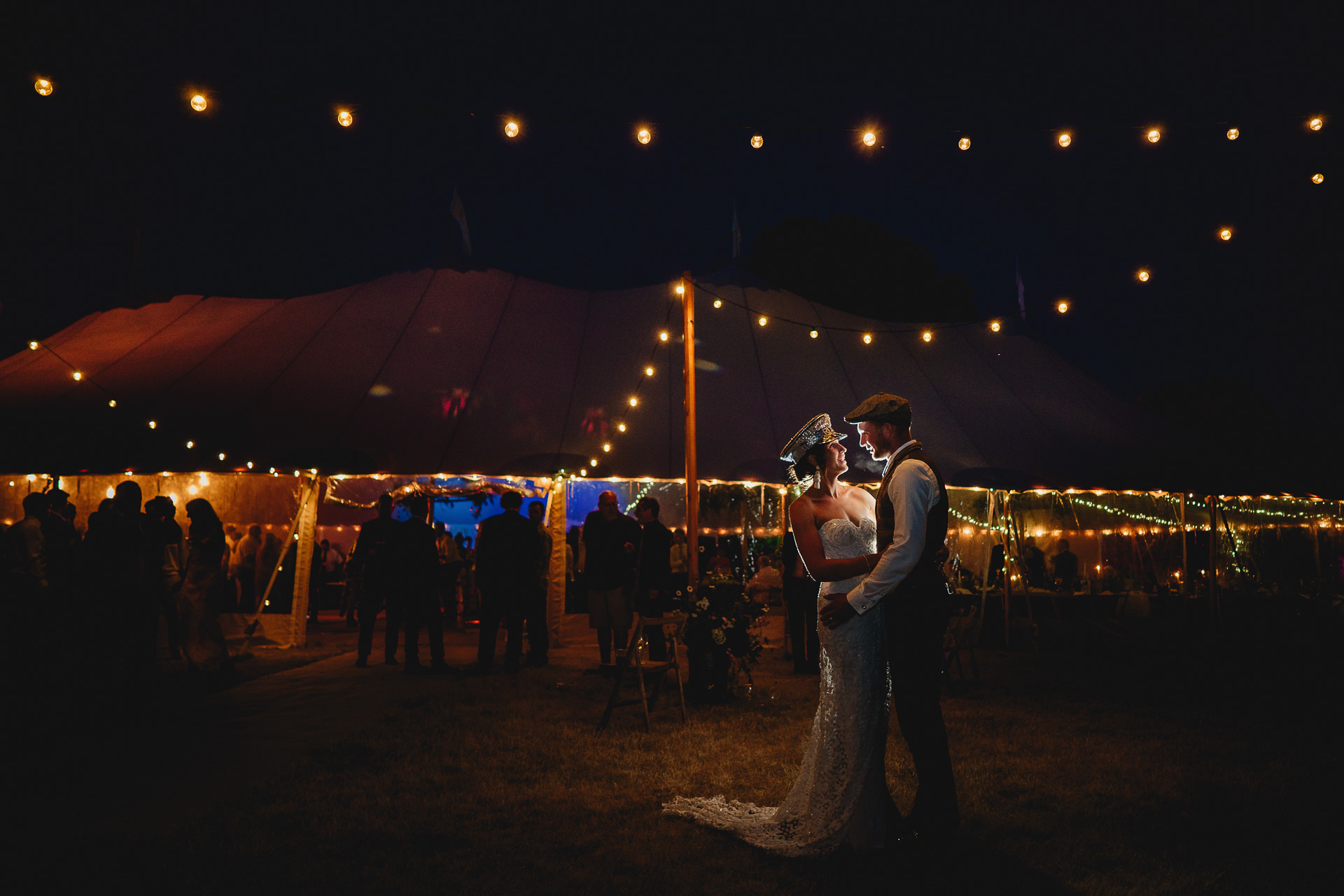 Bride and groom in the dark outside a marquee with festoon lighting around