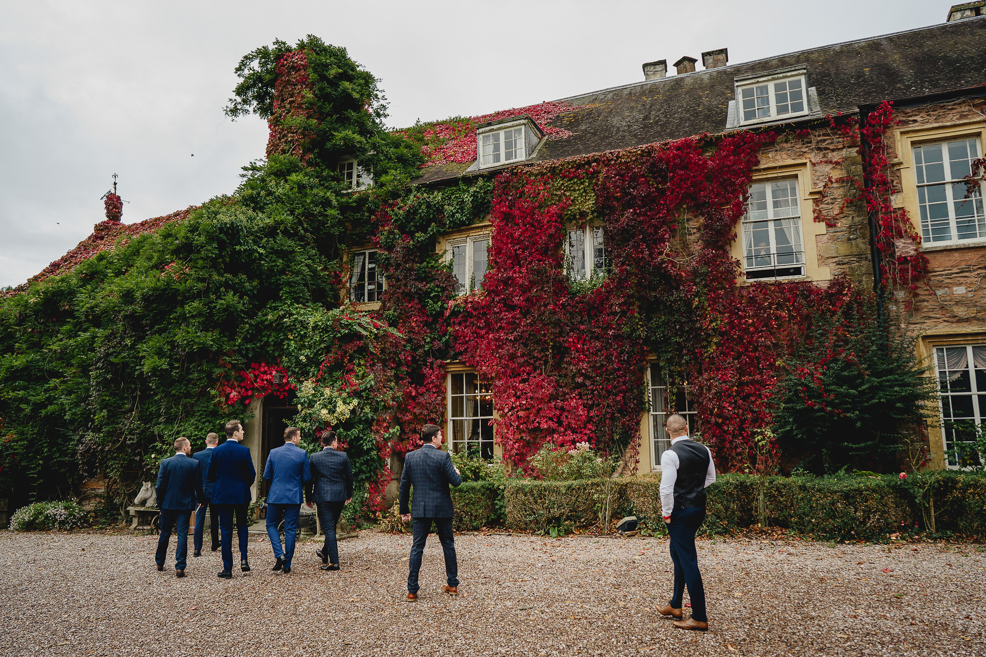 A group of men walking towards a building covered in red Virginia creeper