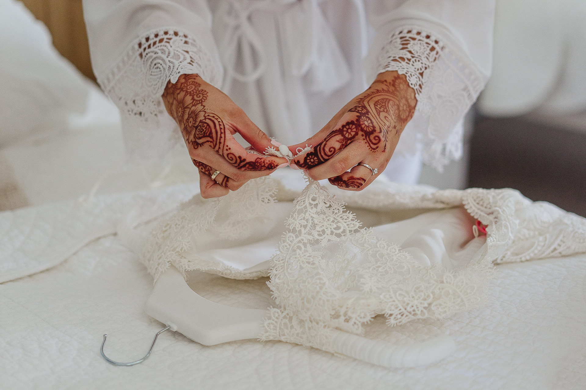 Hennaed hands undoing buttons on a wedding dress