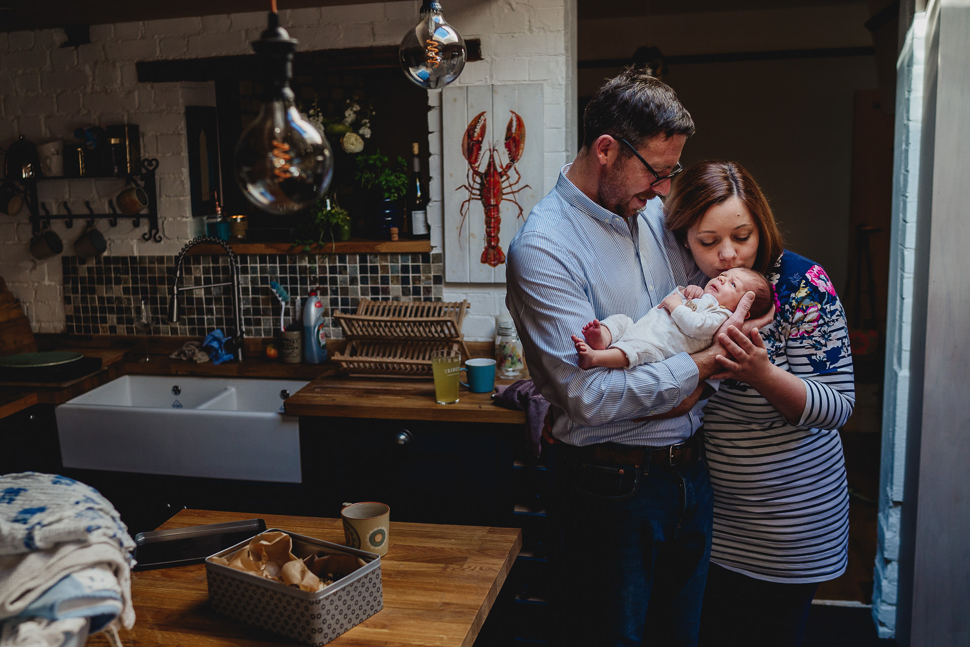 Parents cuddling and kissing a newborn at home in their kitchen