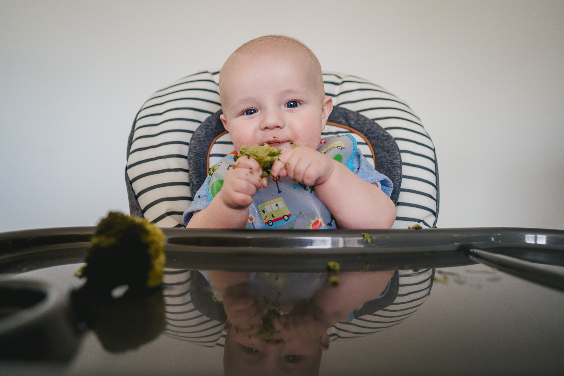 A baby in a high chair eating broccoli