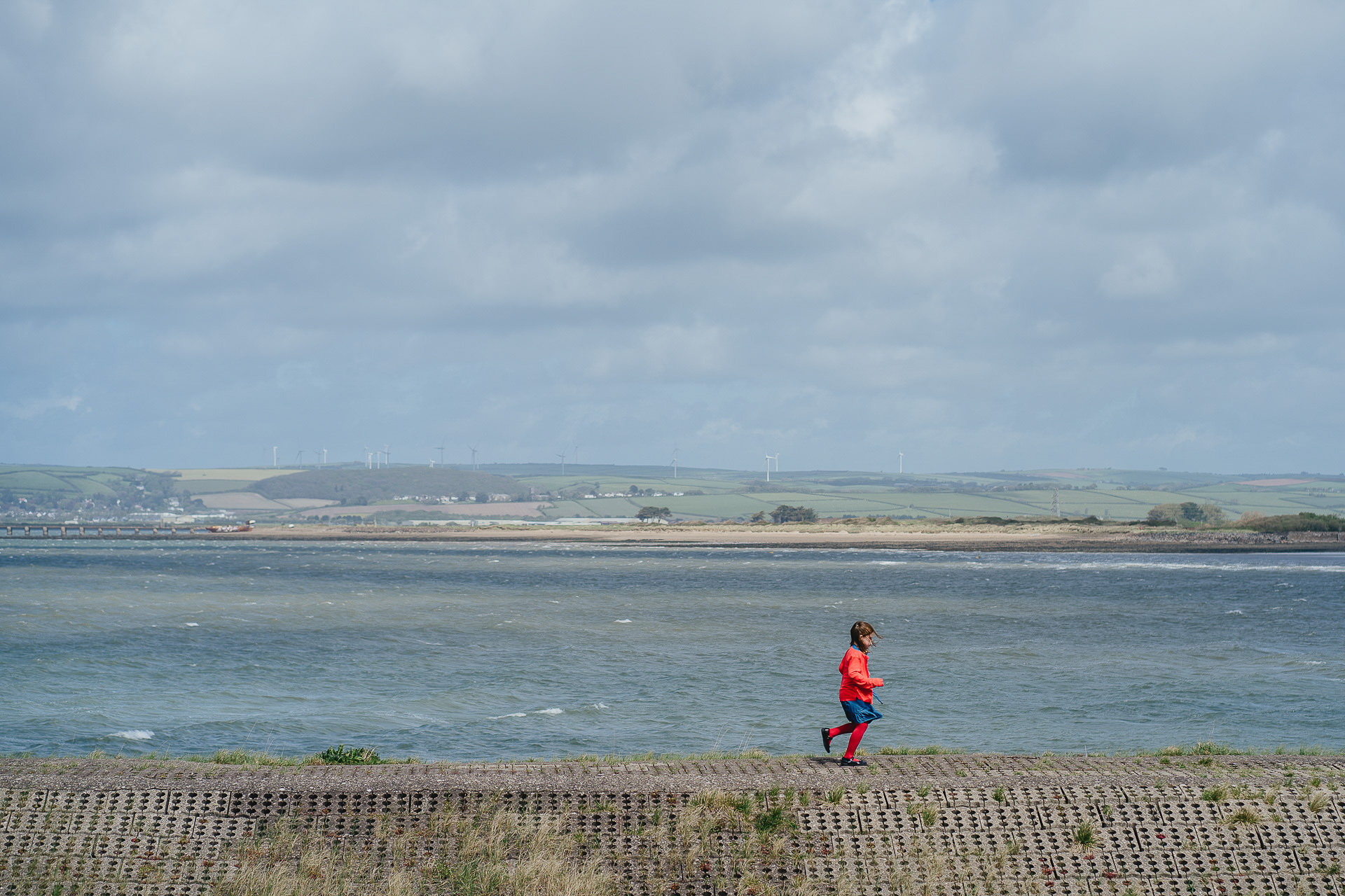 A child dressed in red running in front of the sea