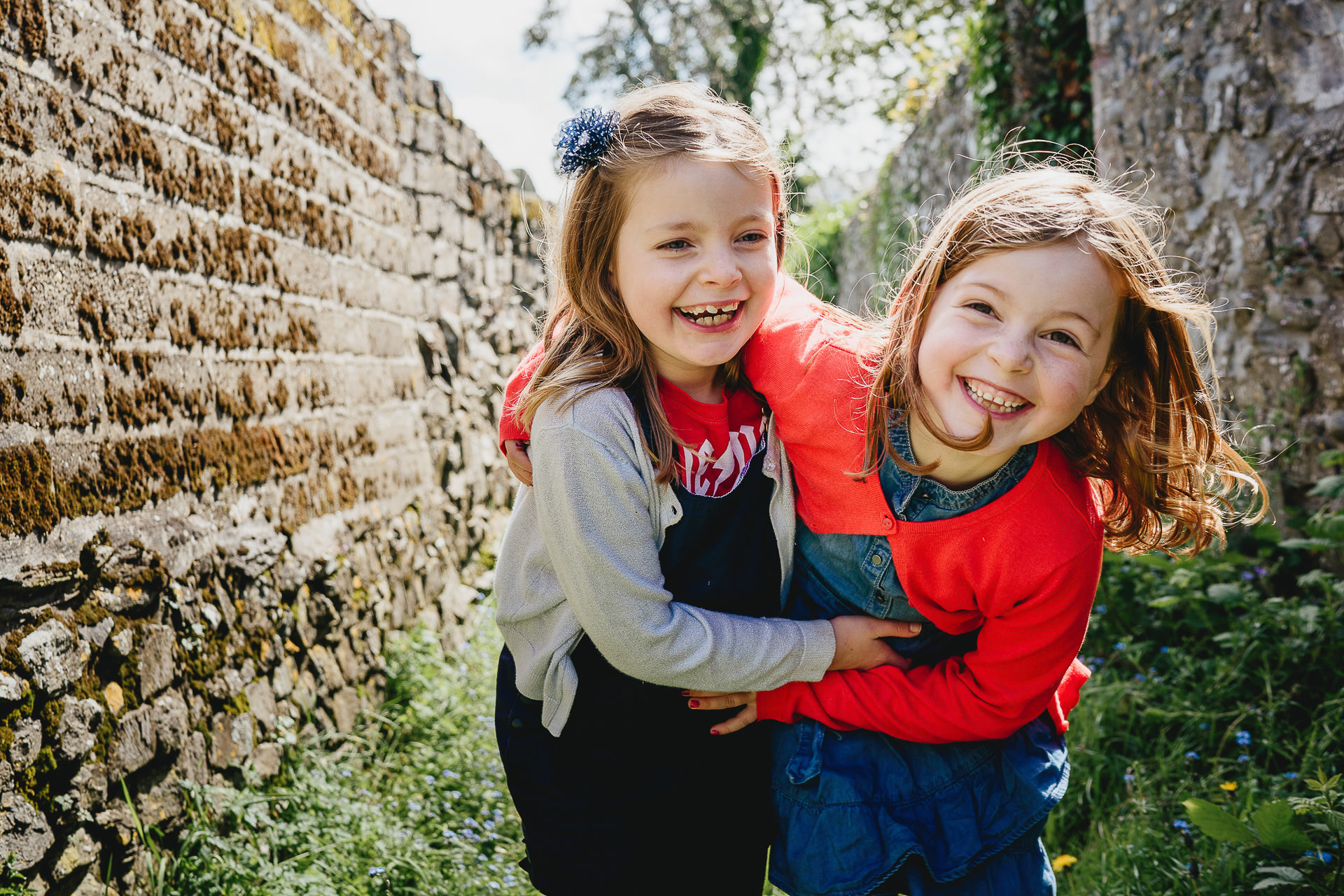 Two girls laughing together in an alleyway with a relaxed family photographer capturing the fun