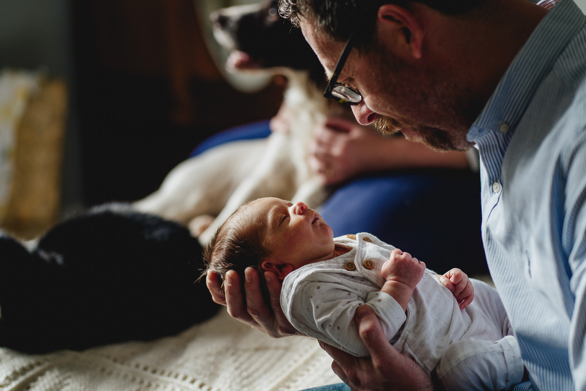 Father looking at a sleeping newborn in his arms whilst relaxing at home