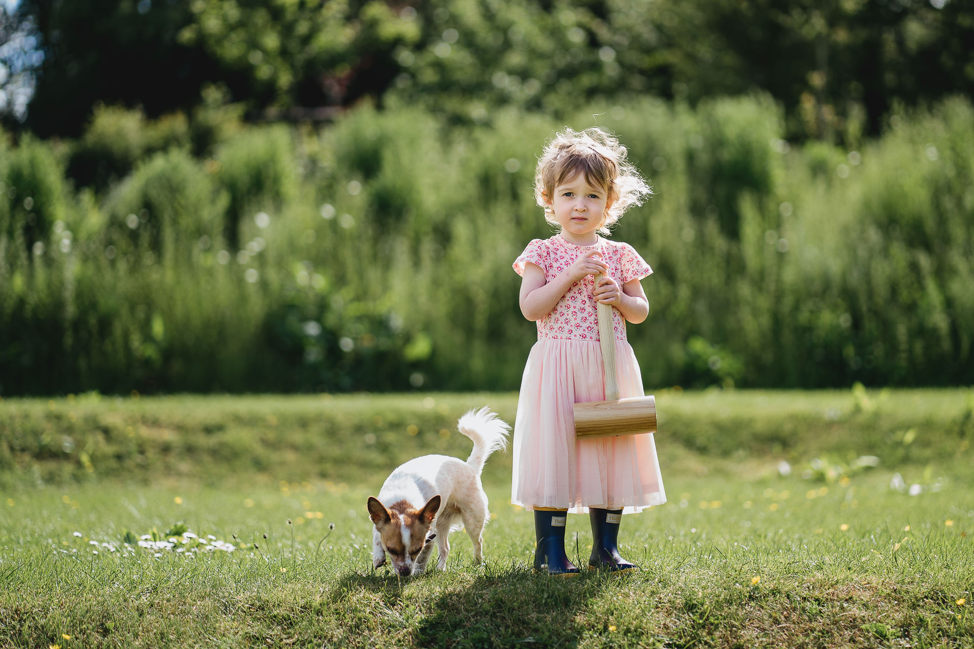 A young girl with a dog on a lawn with a croquet mallet