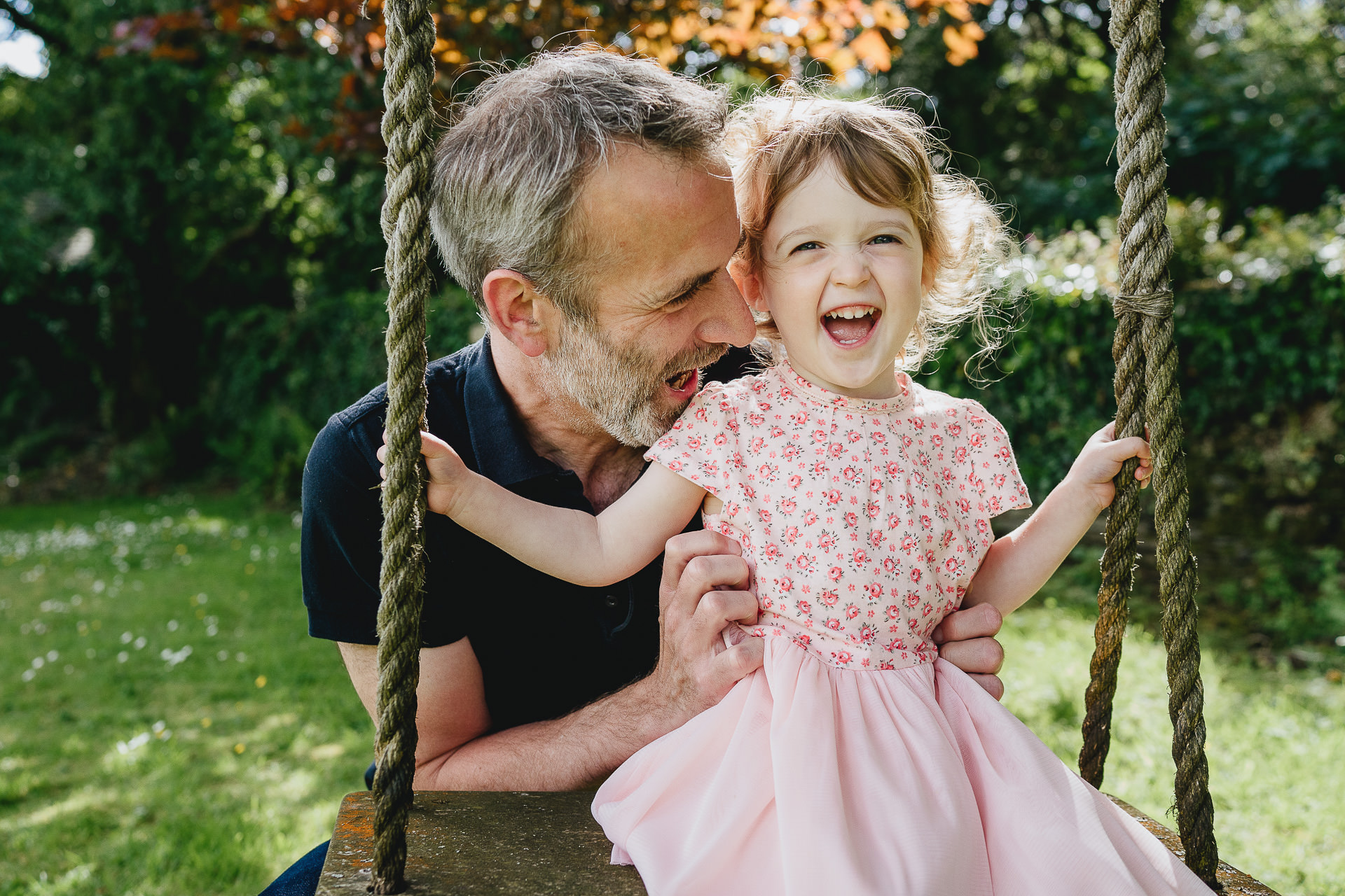 A small girl laughing on a swing with her father