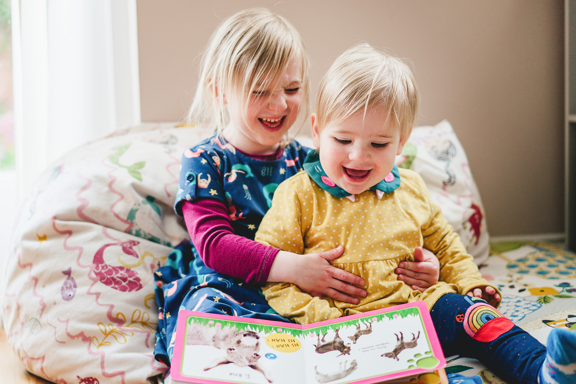 Two sisters laughing at a book together