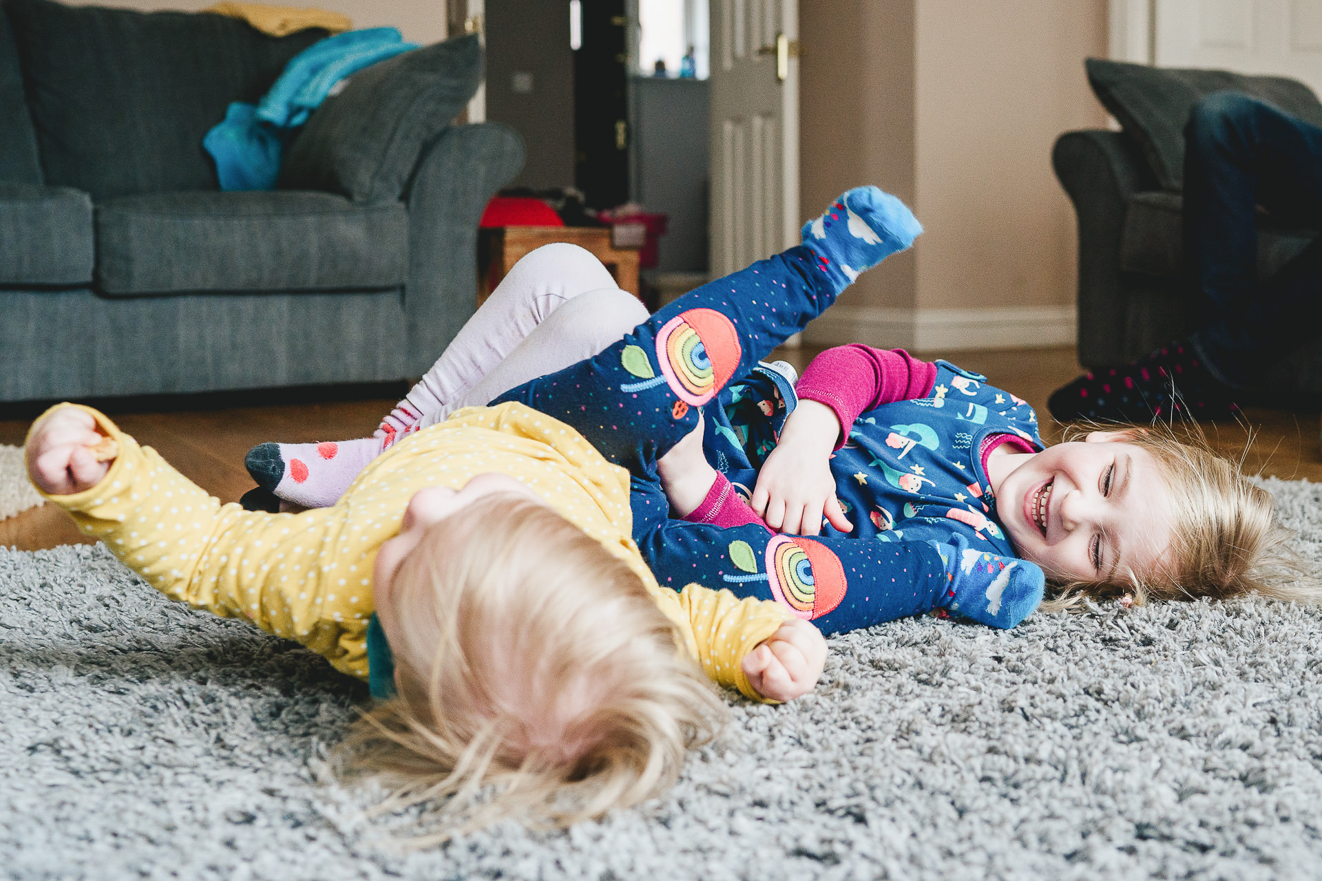 A relaxed family photographer session at home with two children laughing and rolling on the floor together