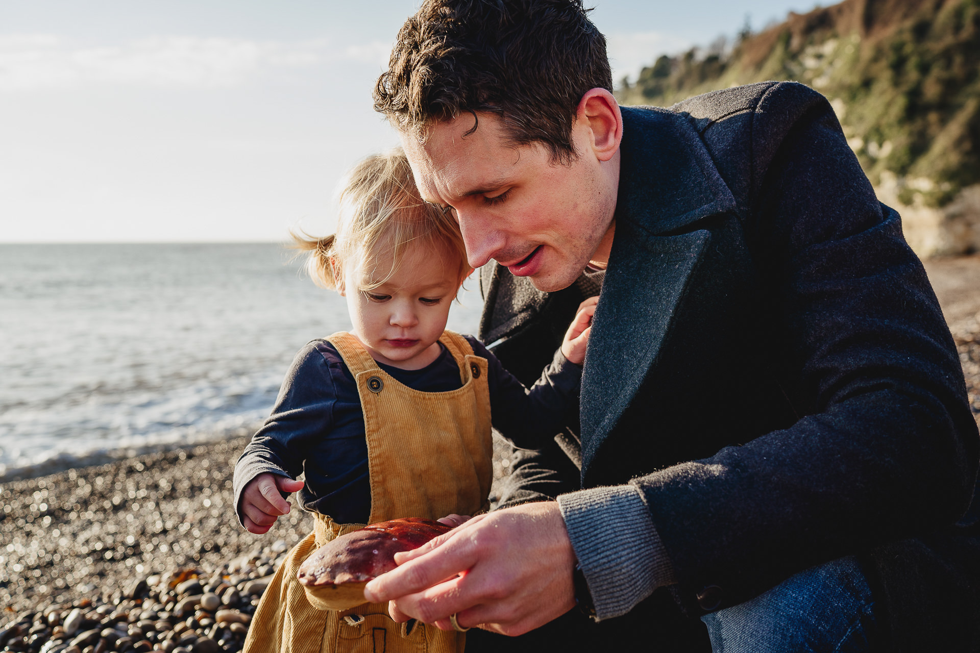 A father and daughter on a beach looking at a crab shell