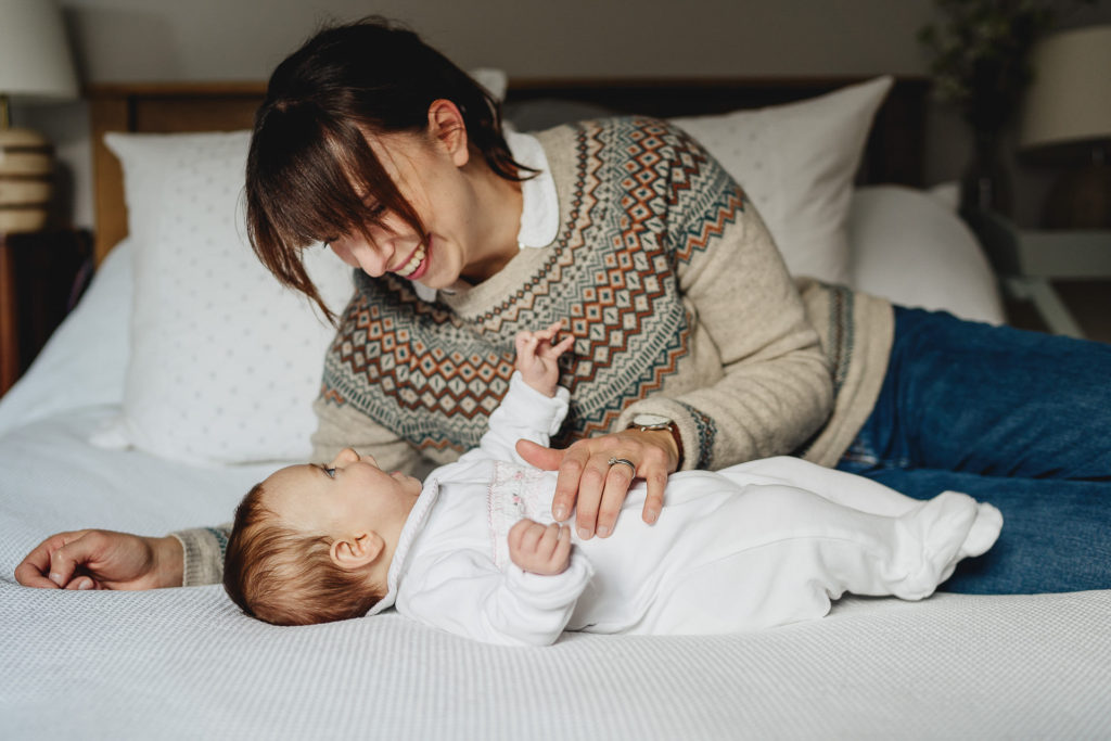 A mother and baby smiling at each other on a bed