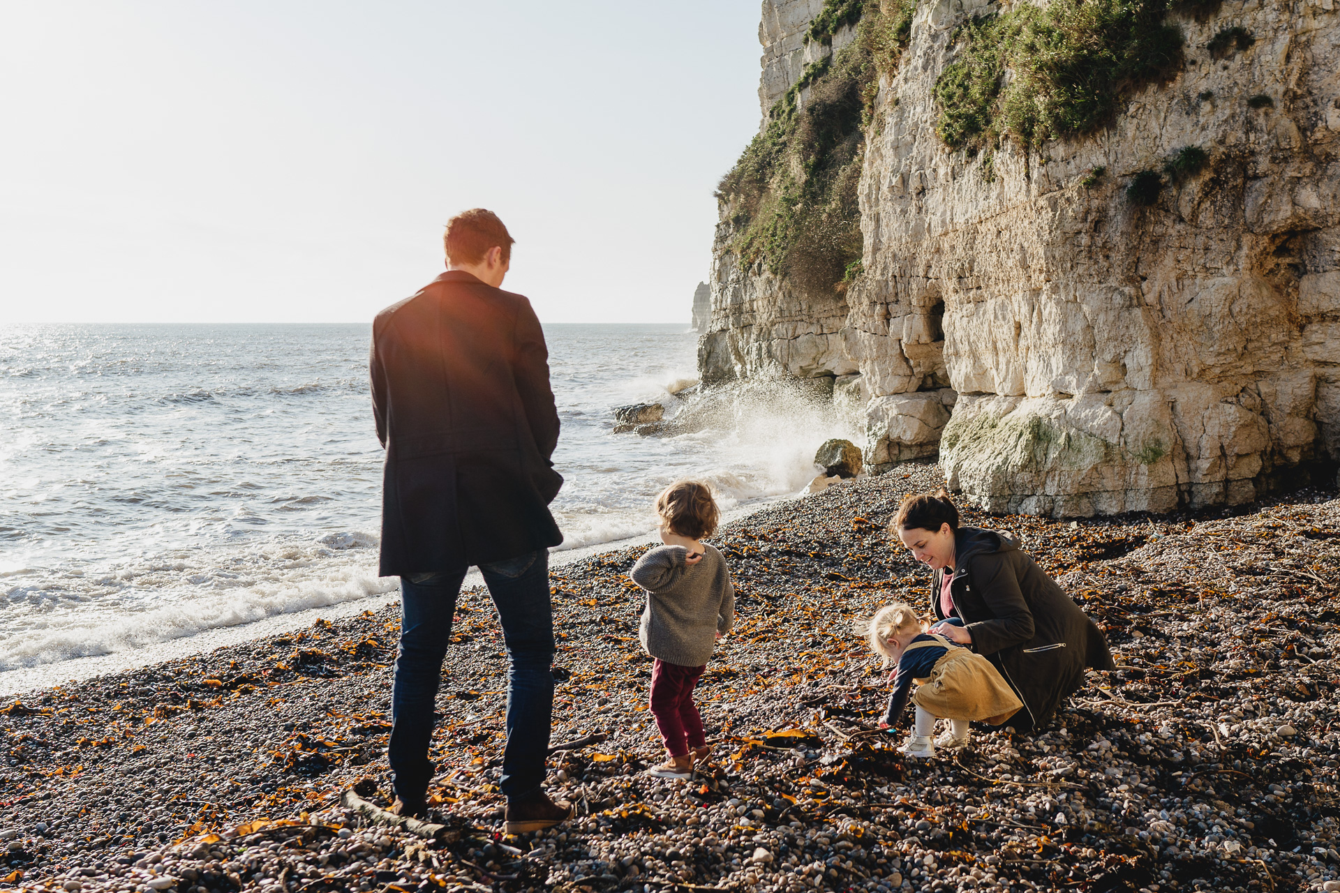 A family with young children on a beach throwing stones into the sea