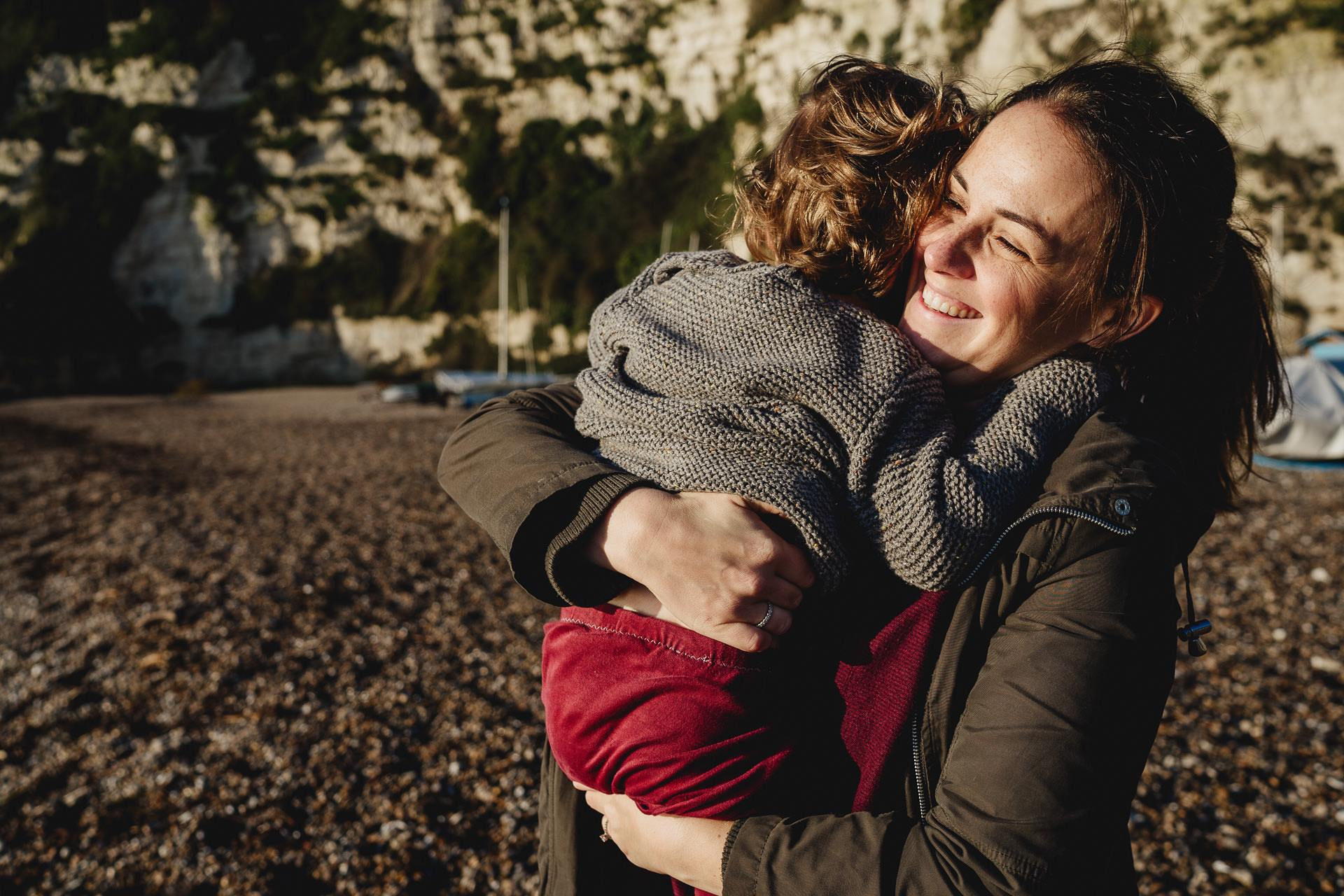 Winter family photography of a mother smiling and cuddling her son on a beach
