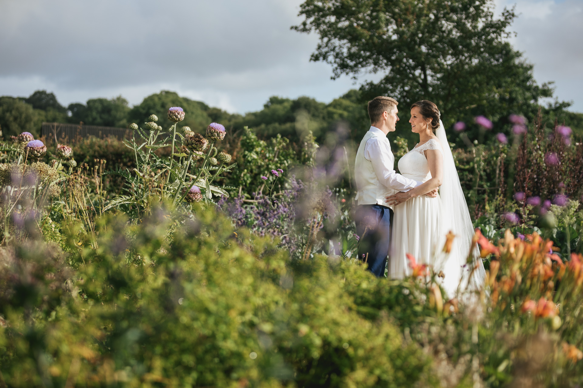 A bride and groom together in a kitchen garden surrounded by flowers and plants. 