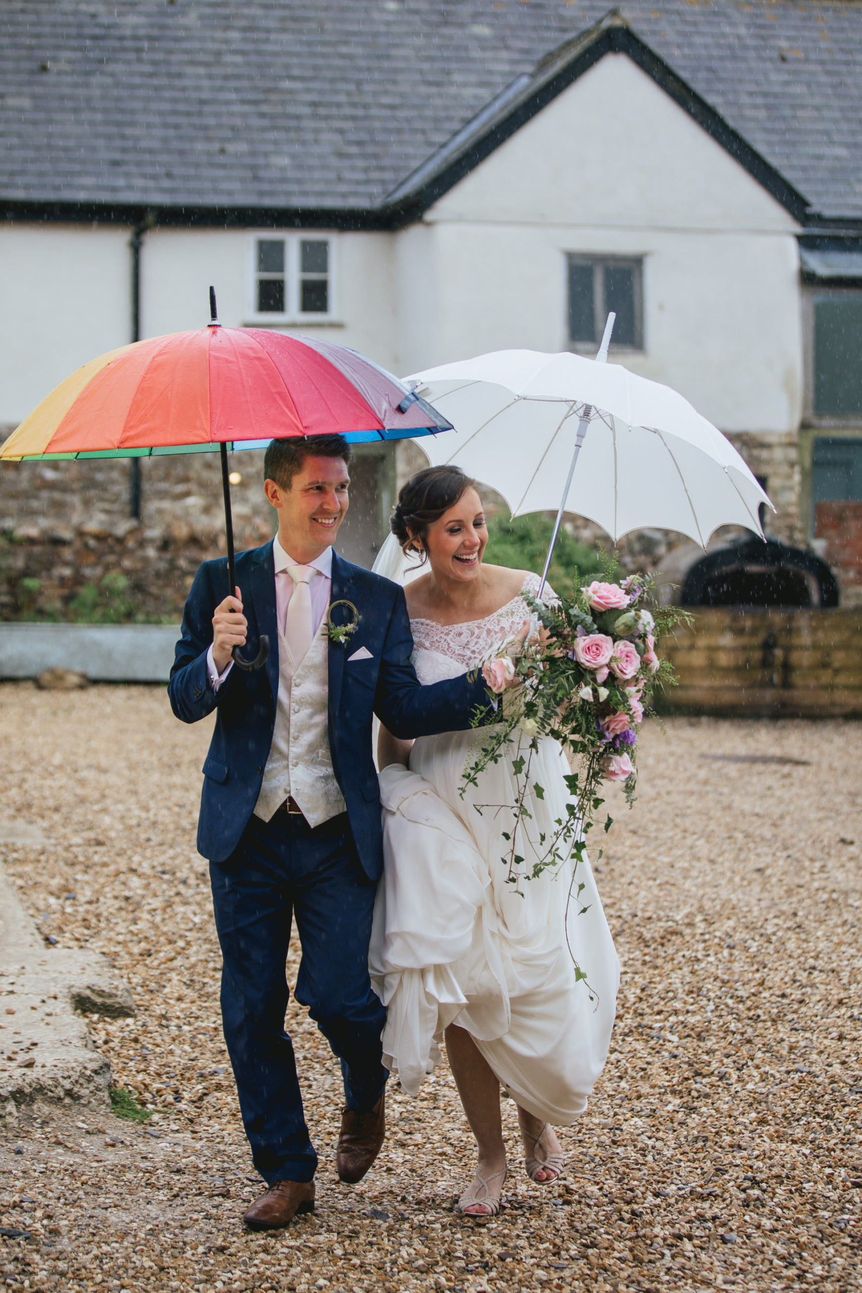 Bride and groom smiling under an umbrella on a rainy wedding day 