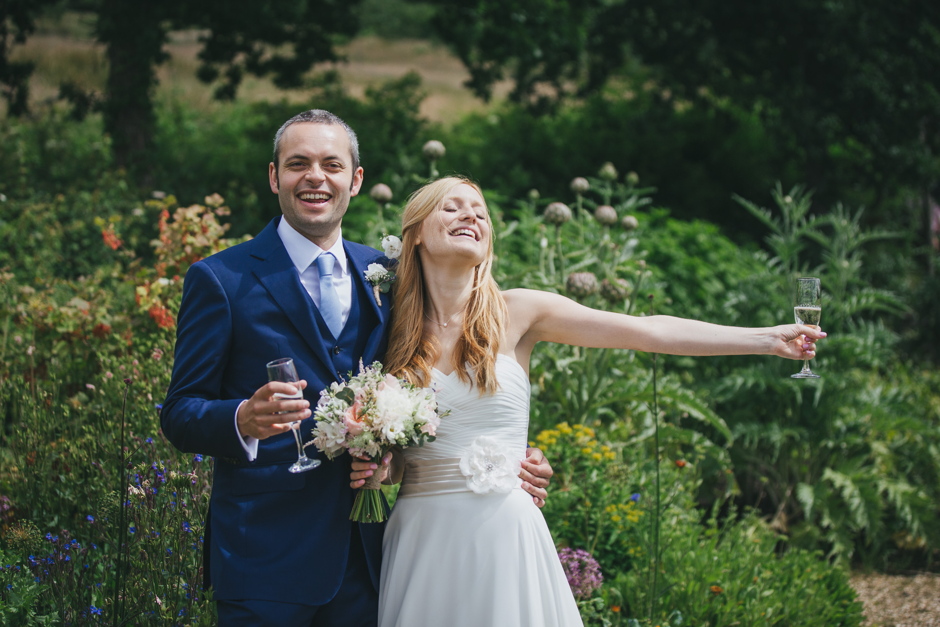 A bride and groom smiling in a garden with champagne in their hands