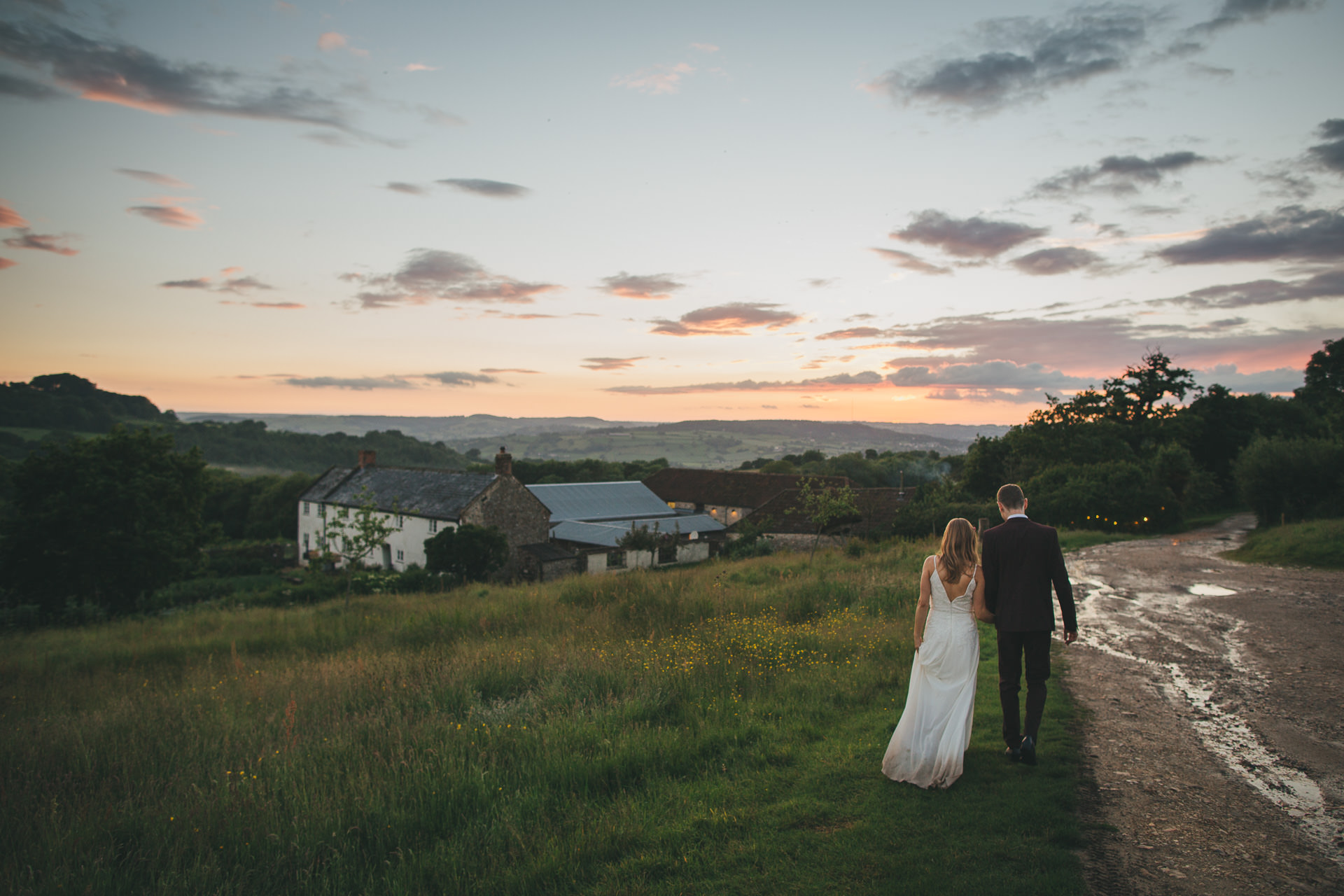 Bride and groom walking down a hill in a sunset after a wet weather wedding. 