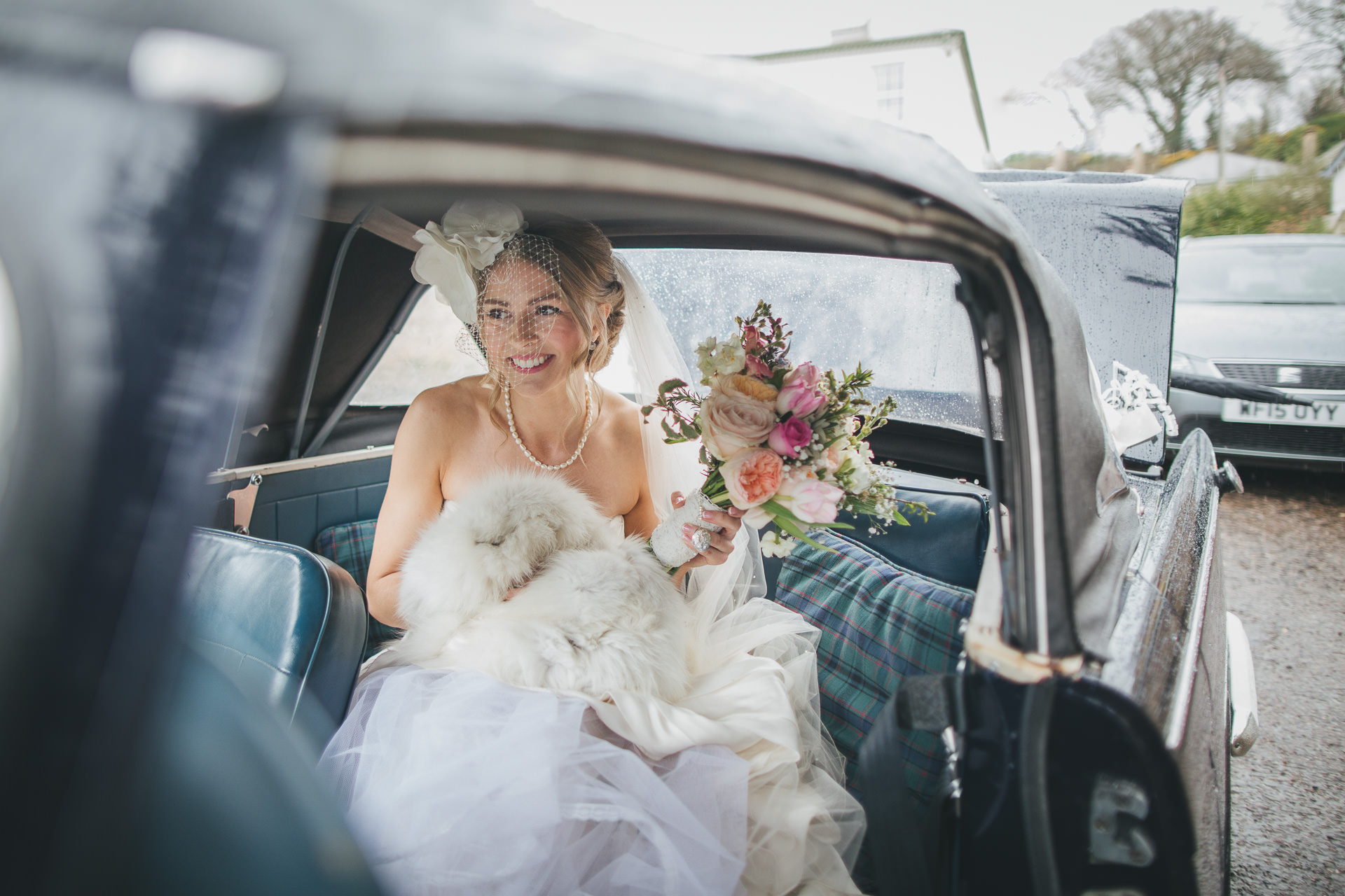 A bride arriving for her rainy day wedding, smiling in the wedding car. 