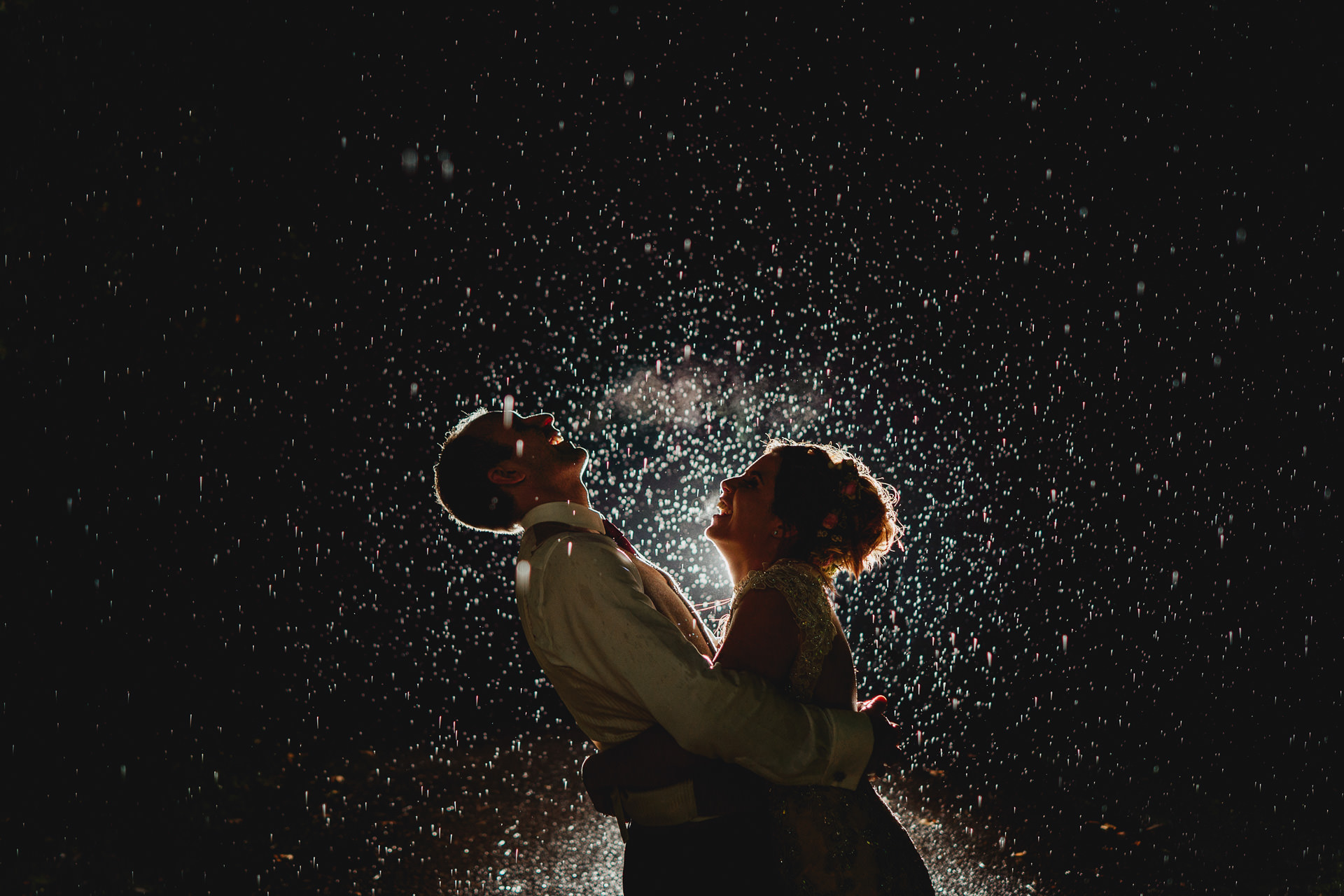 Bride and groom laughing in the rain together at night