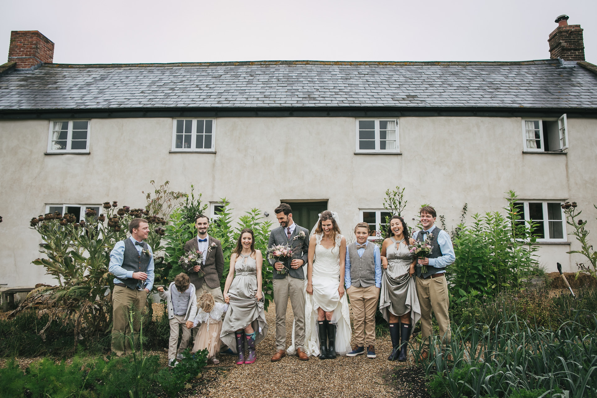 A group photo with the bride and groom with their wedding party all wearing wellies and laughing. 
