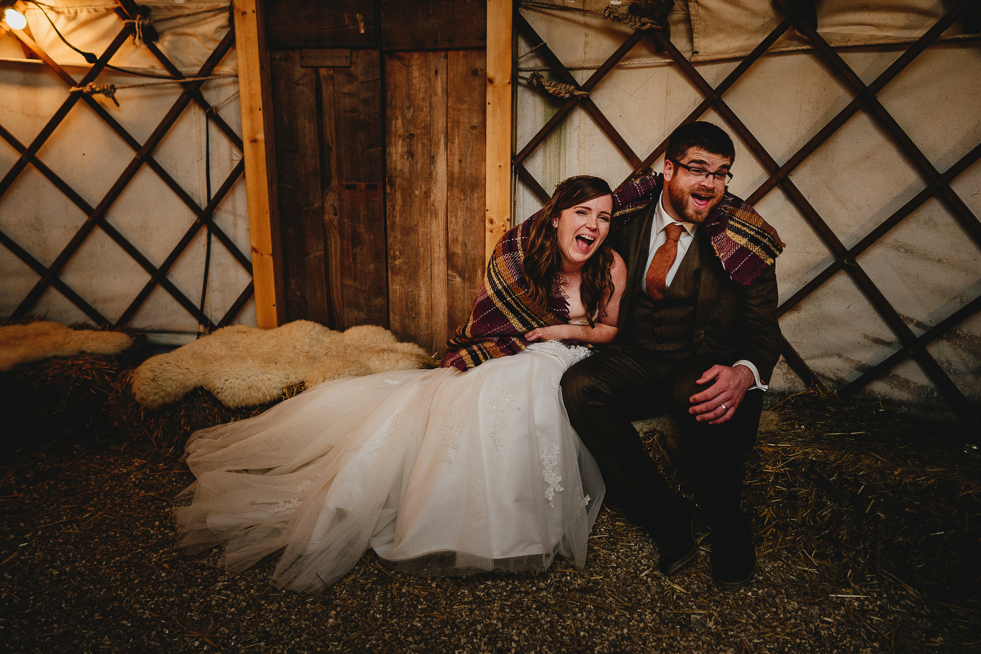 A bride and groom wrapped in a blanket and laughing
