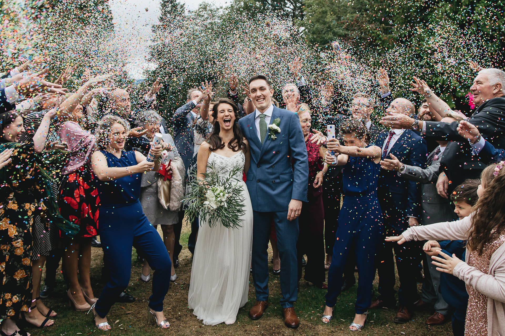 Bride and groom surrounded by wedding guests throwing confetti
