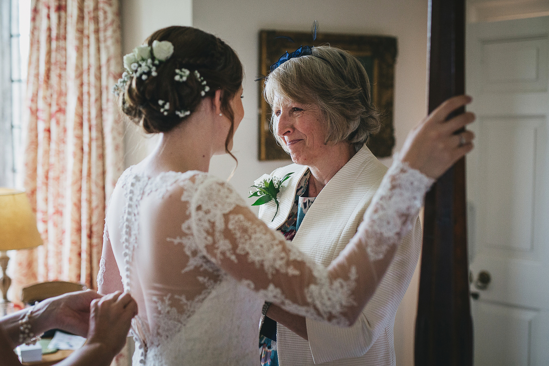 Mother smiling proudly at bride whilst fastening dress