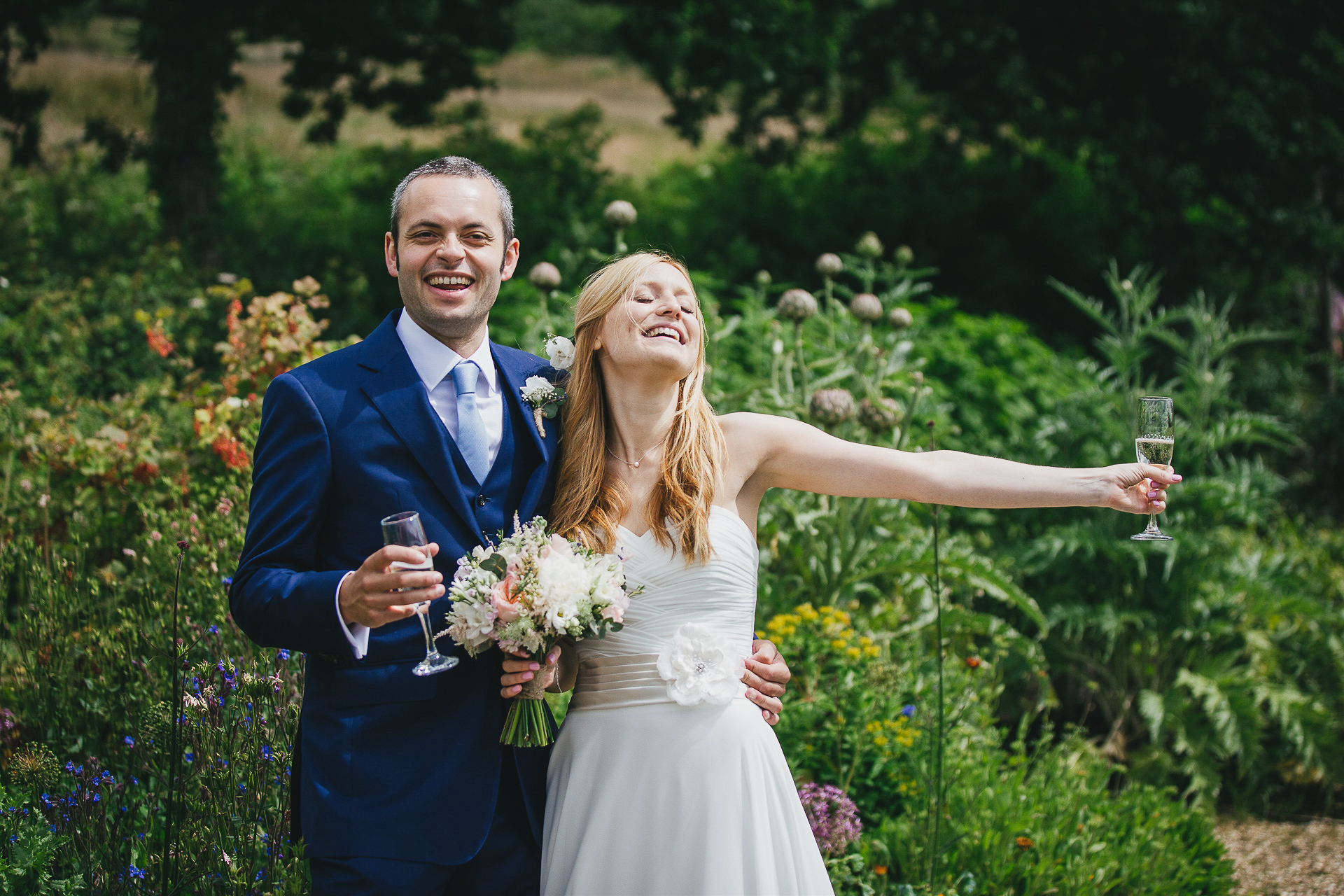 Bride and groom looking happy with champagne in a garden