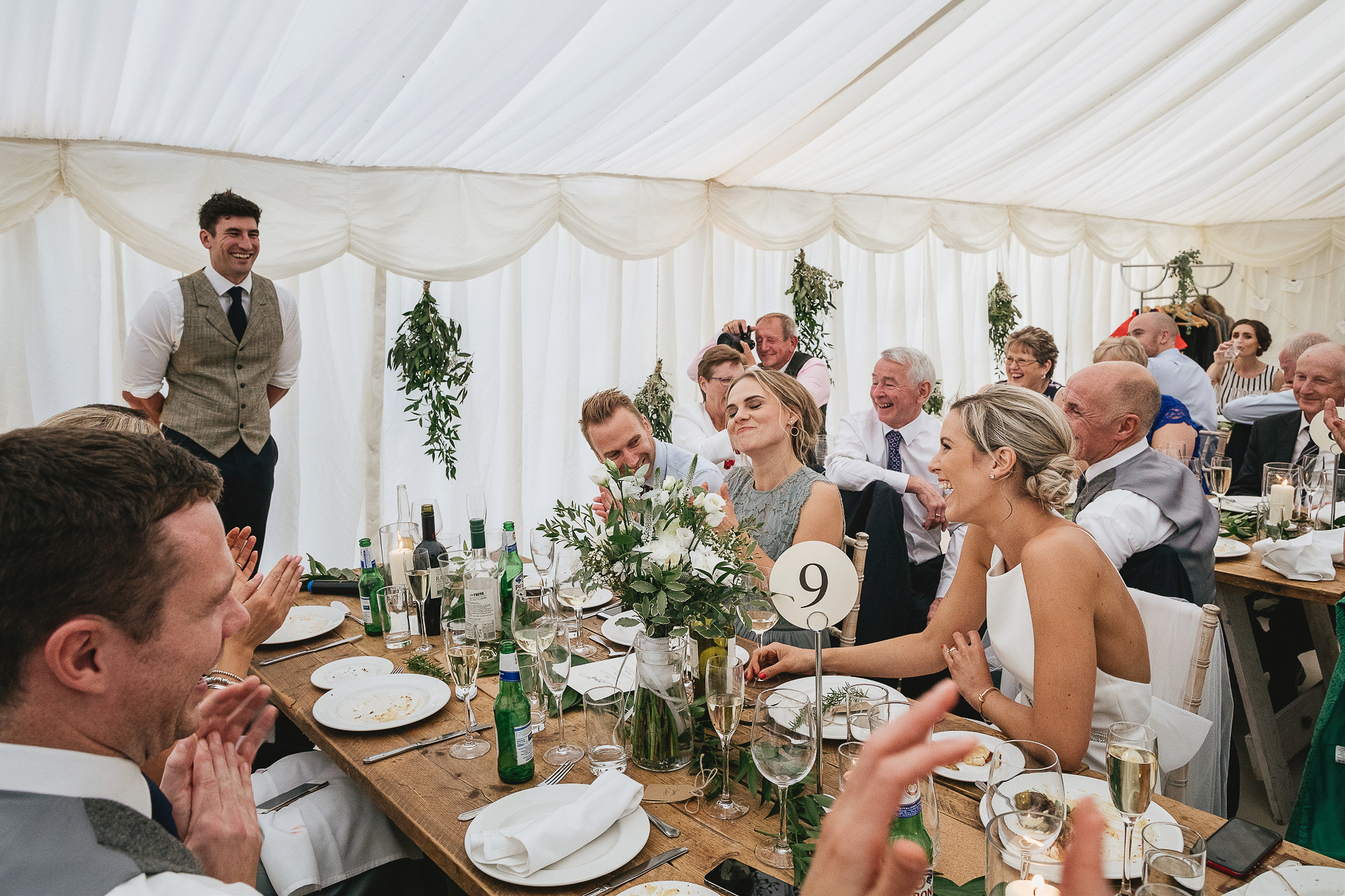 Bride and groom laughing together during speeches in a marquee