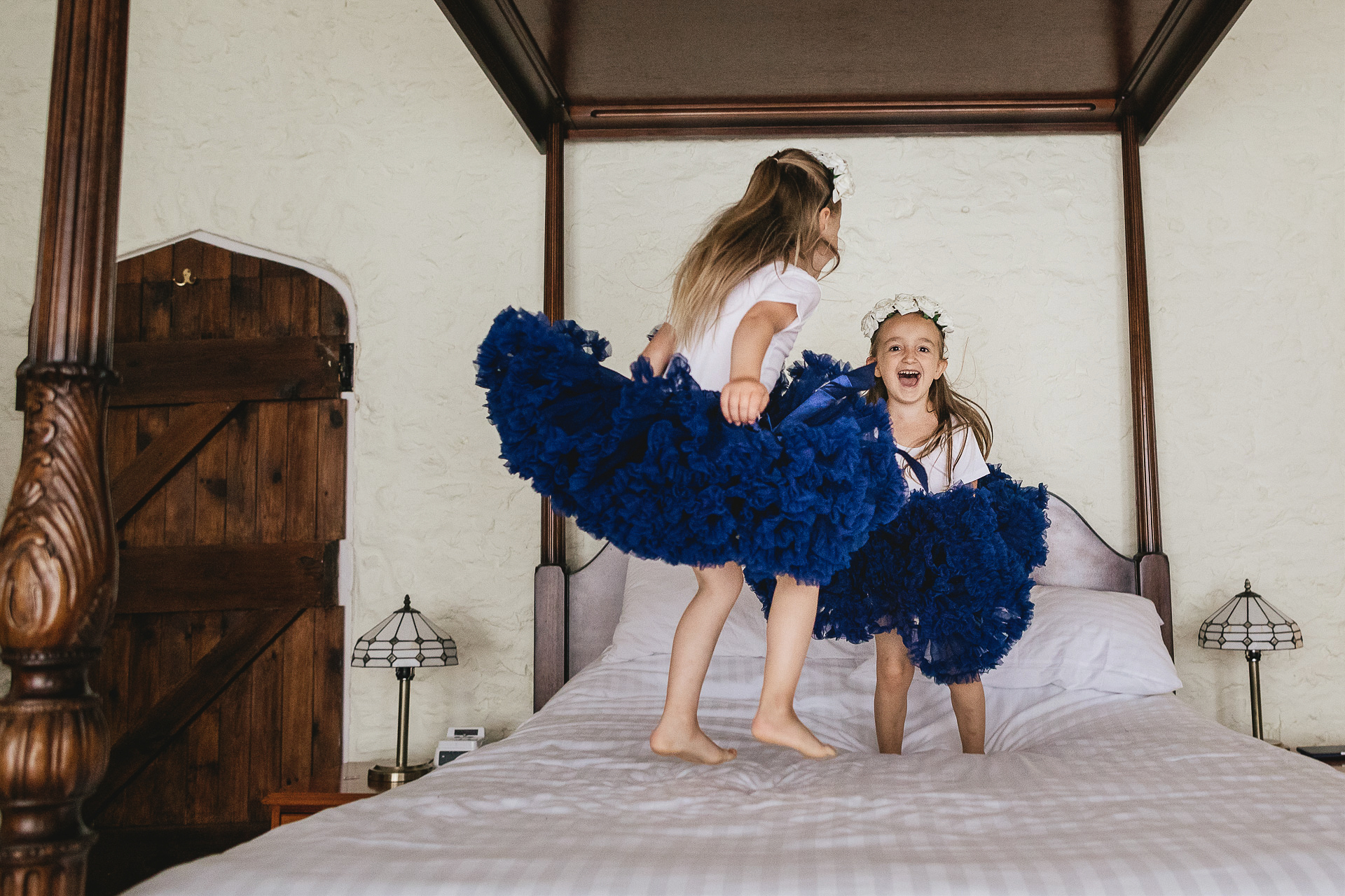 Flower girls in blue tutus bouncing on a four poster bed