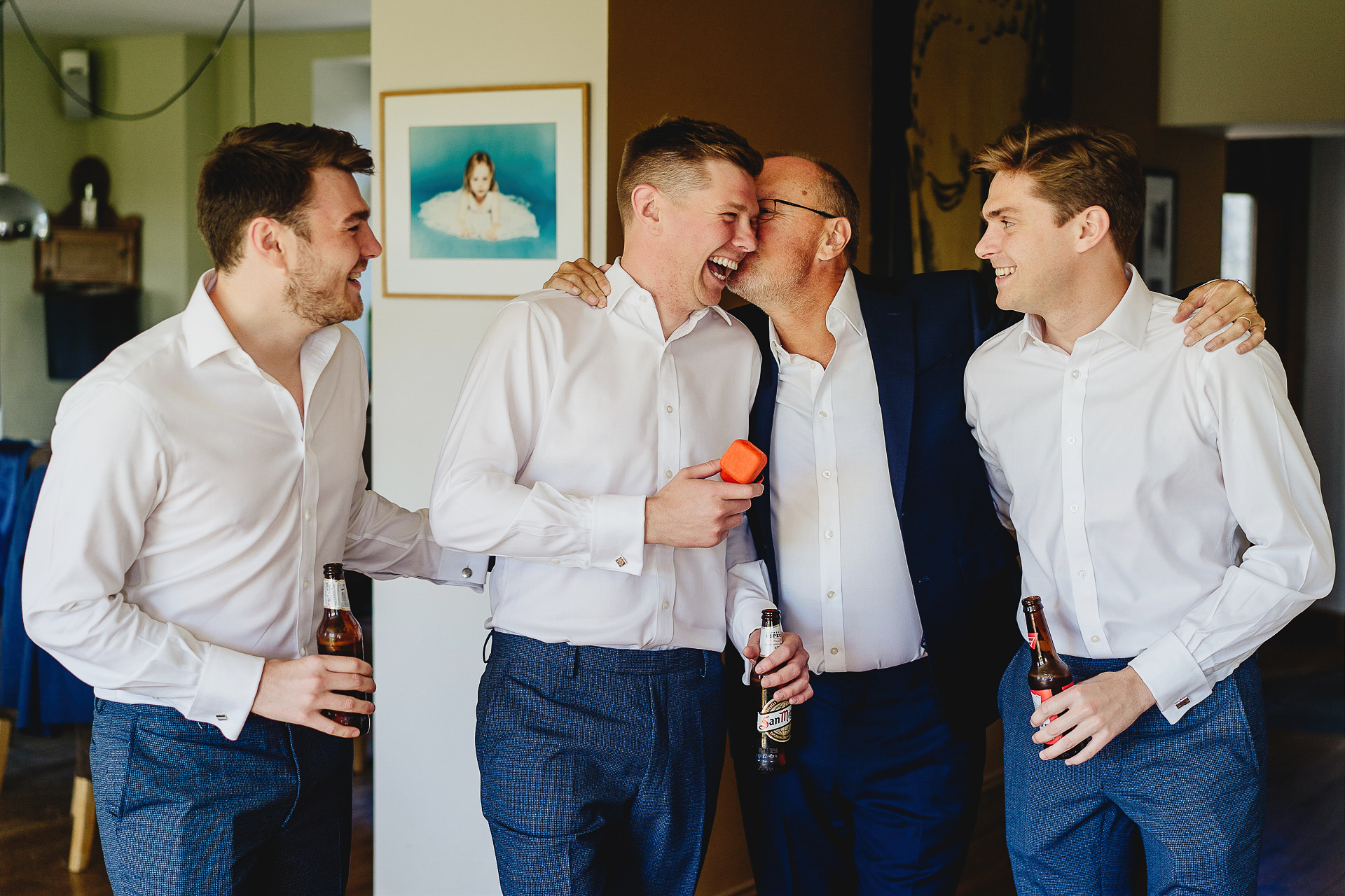 Father kissing groom with brothers watching