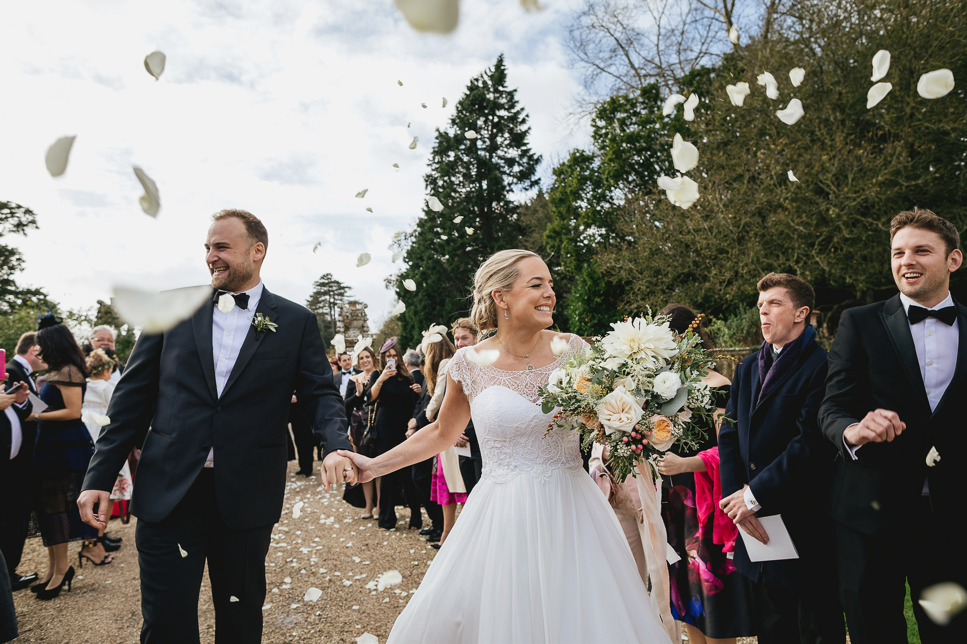 Elegant bride and groom smiling through rose petal confetti