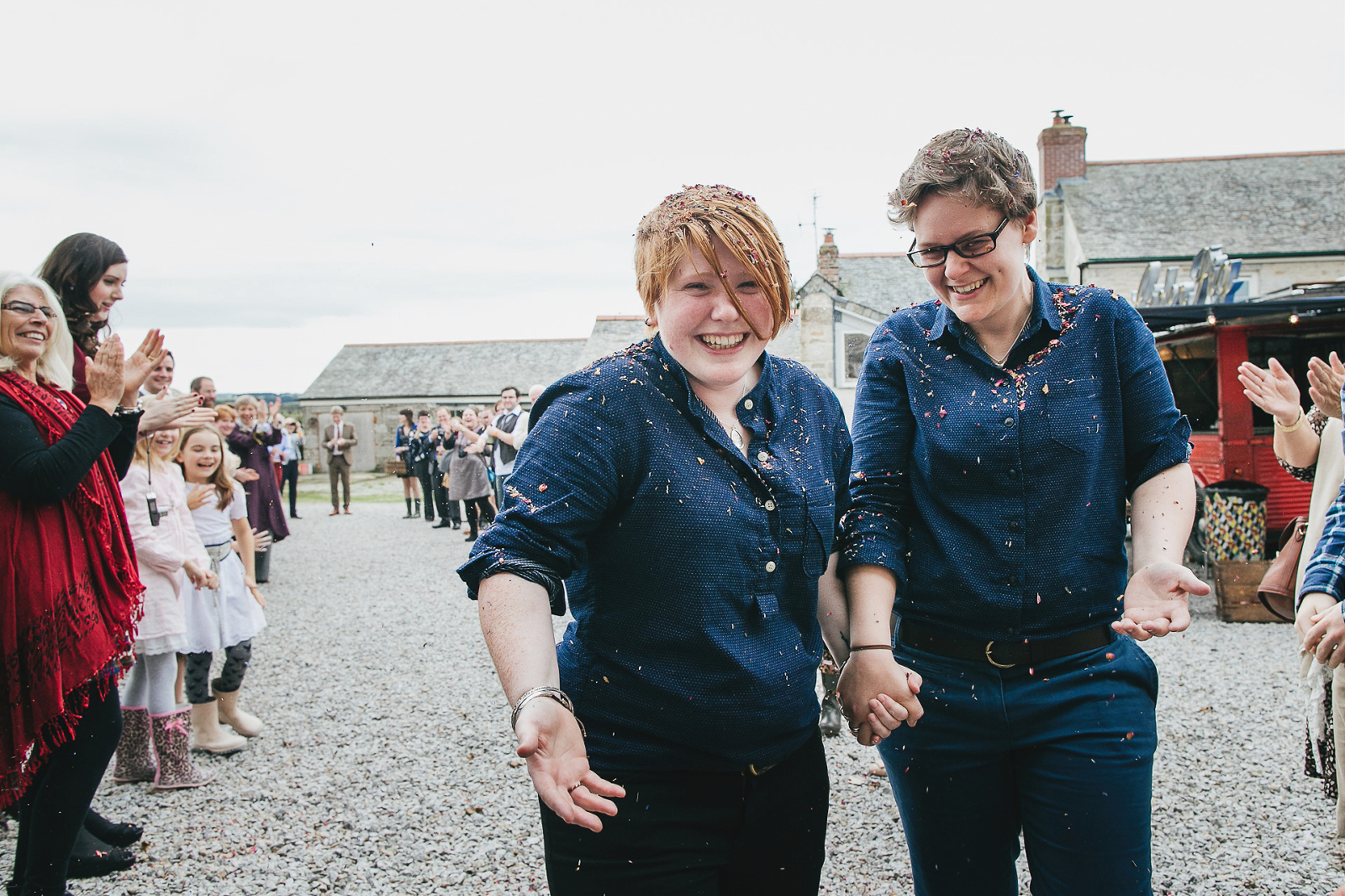 Two smiling brides in blue shirts covered in confetti